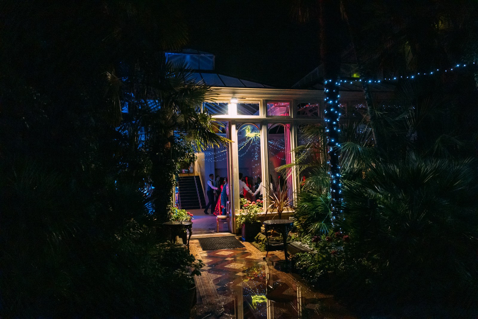 The glowing conservatory at Hampton Court House seen through the night garden