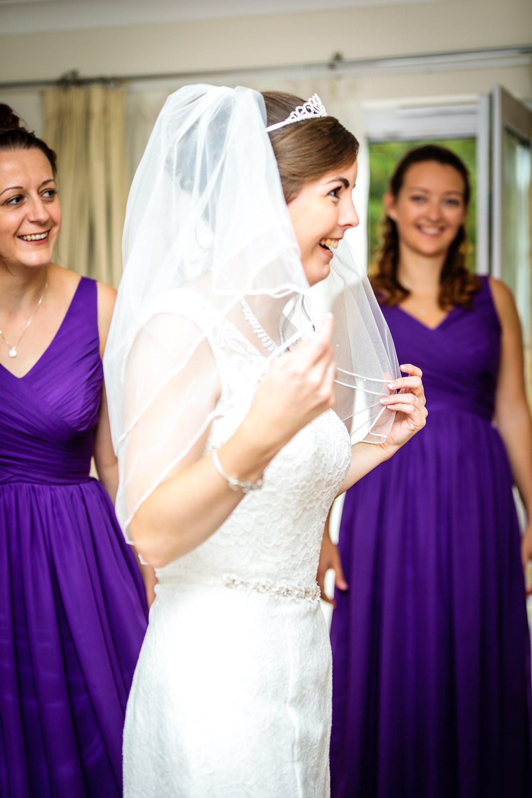 Bridesmaids in purple settling the bride's veil into place