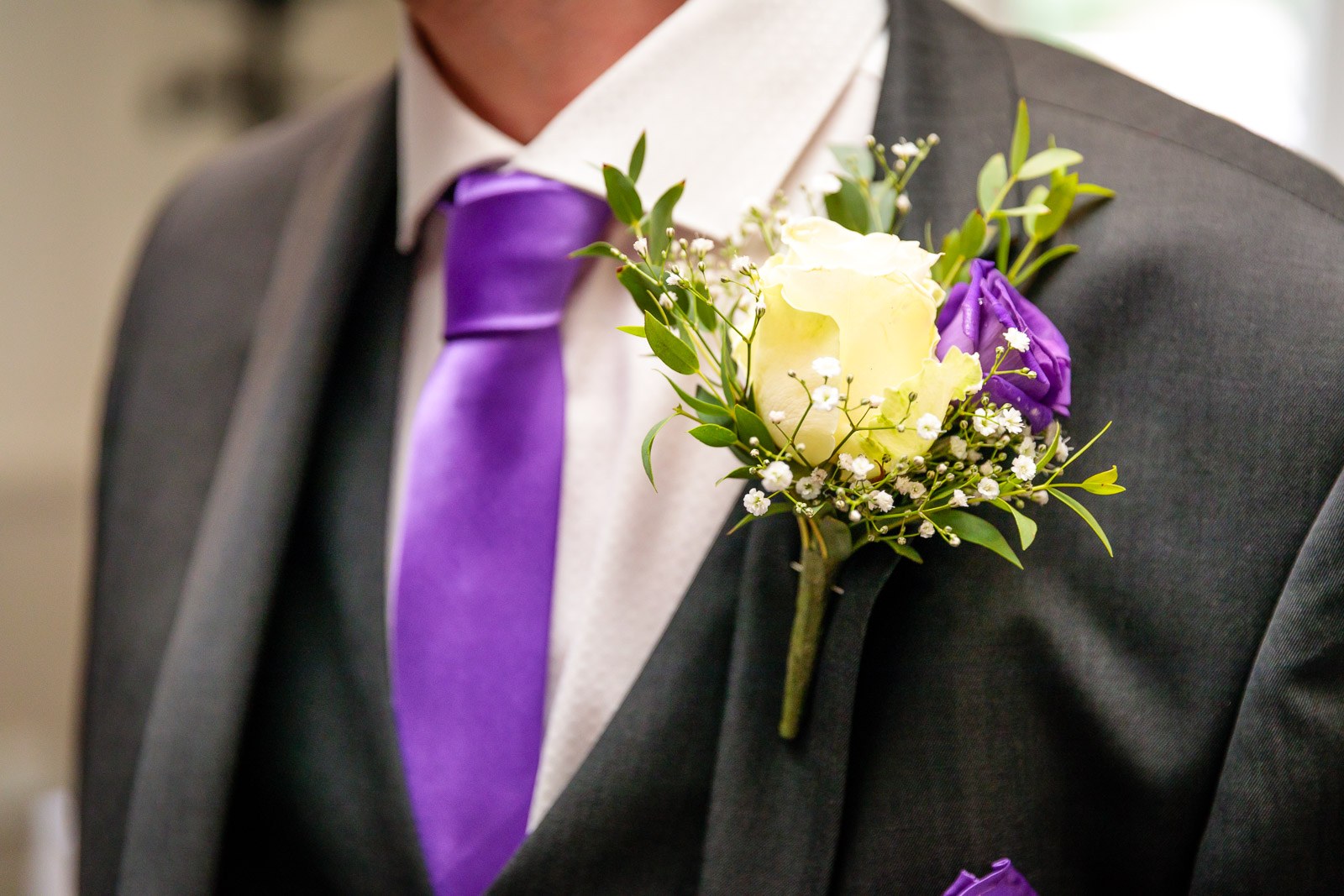 Close-up of the groom's grey suit with a purple tie and rose buttonhole