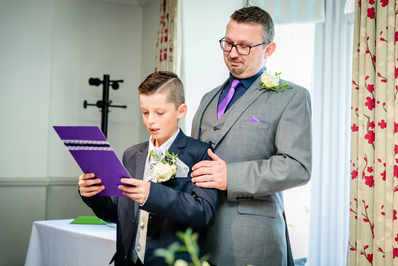 A page boy reading from a purple order of service beside the groom