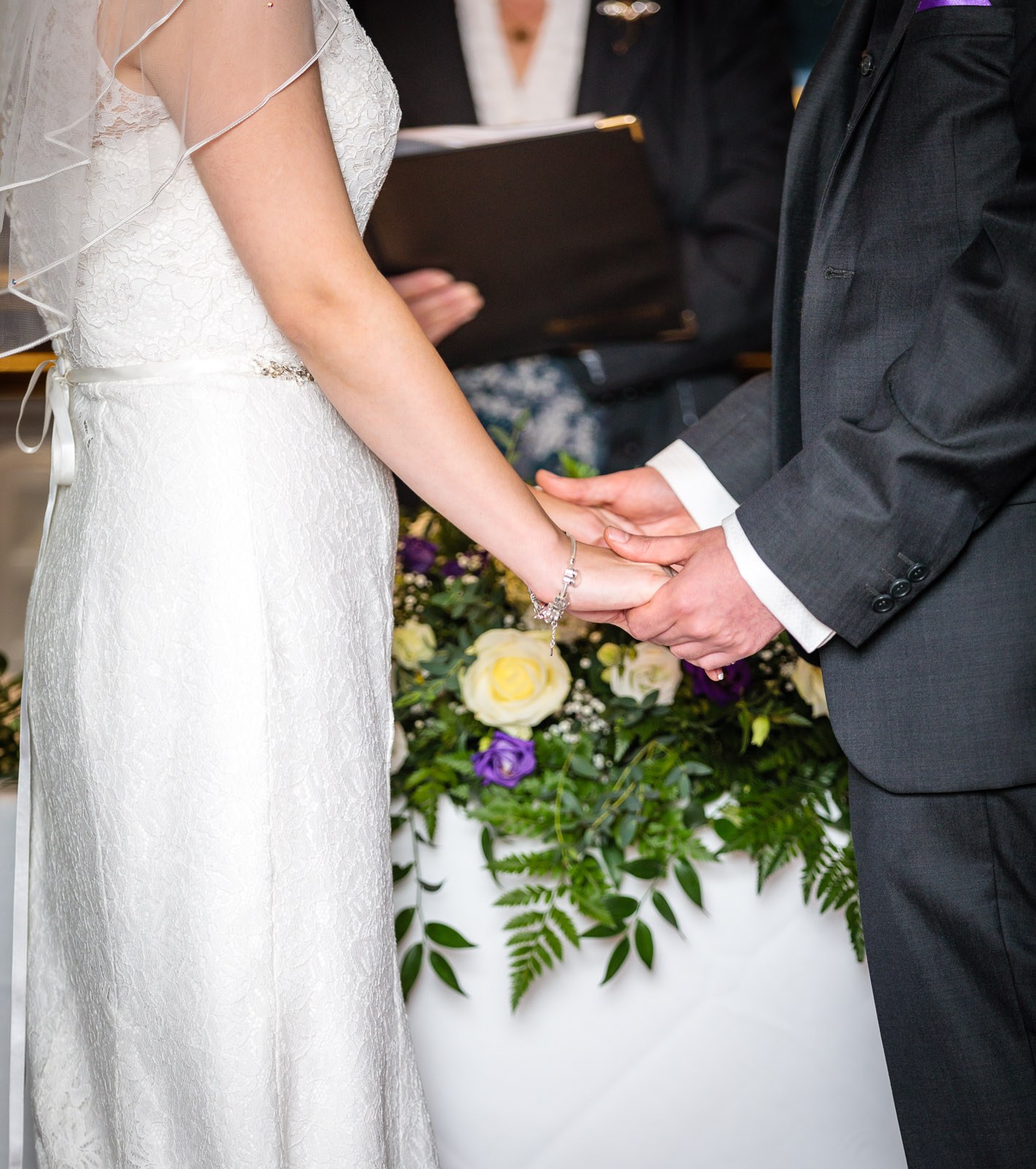 Close-up of the couple's clasped hands over the bouquet during the vows