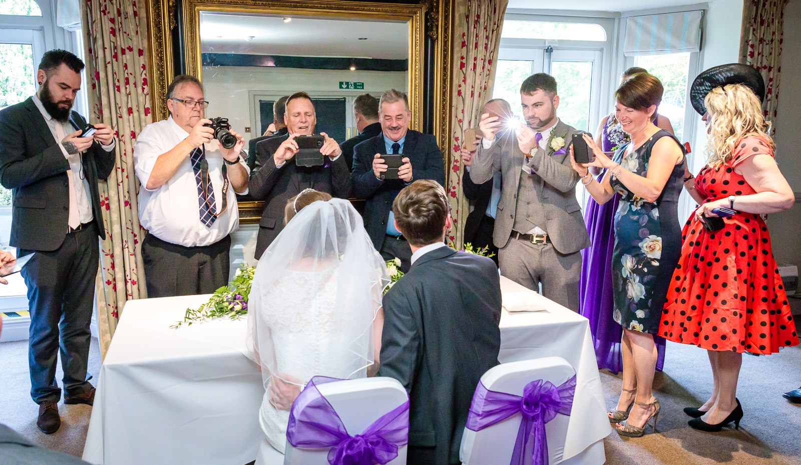 The couple signing the register as guests lean in to photograph the moment