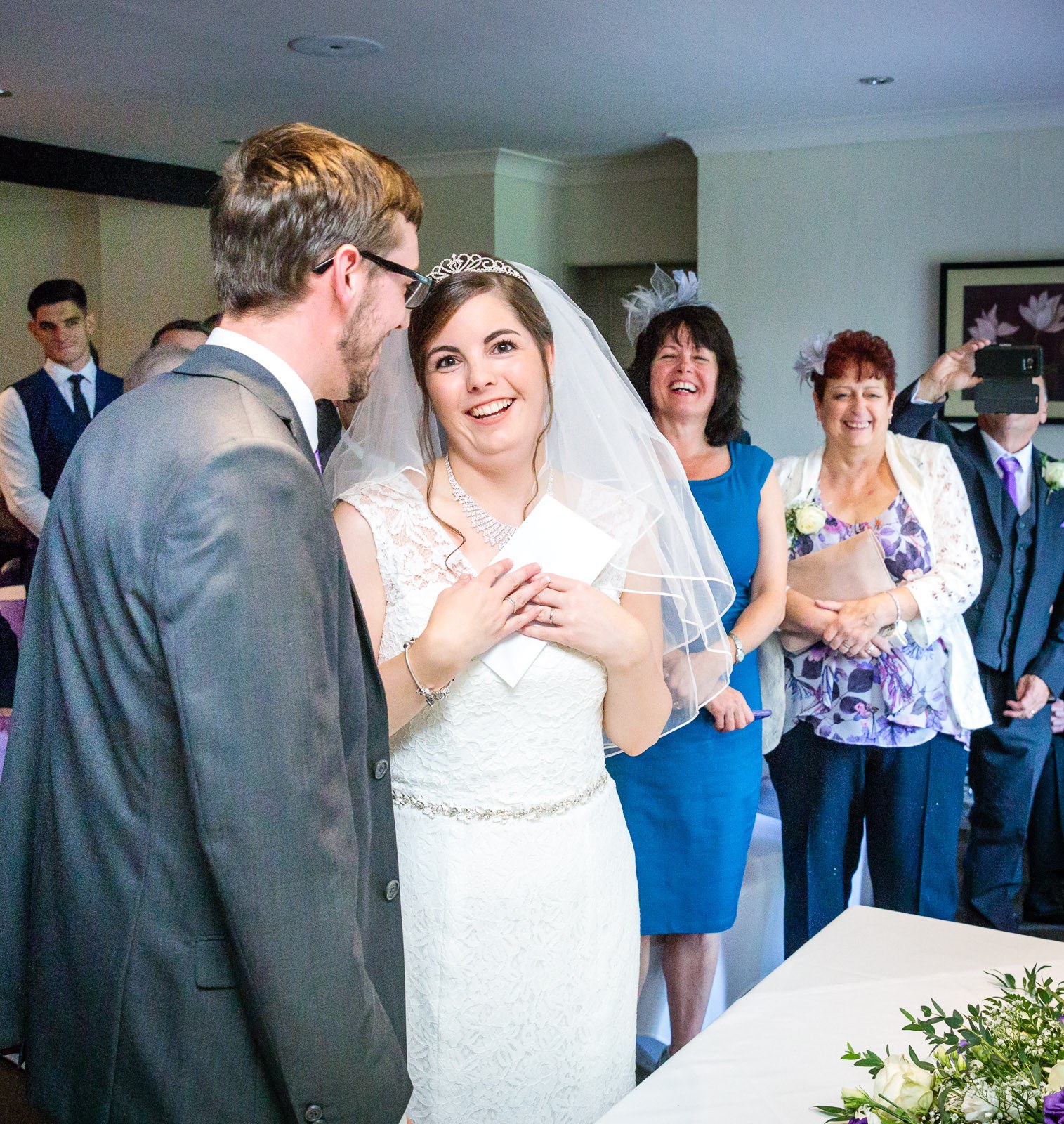 Bride with a hand to her chest, moved, as guests look on behind