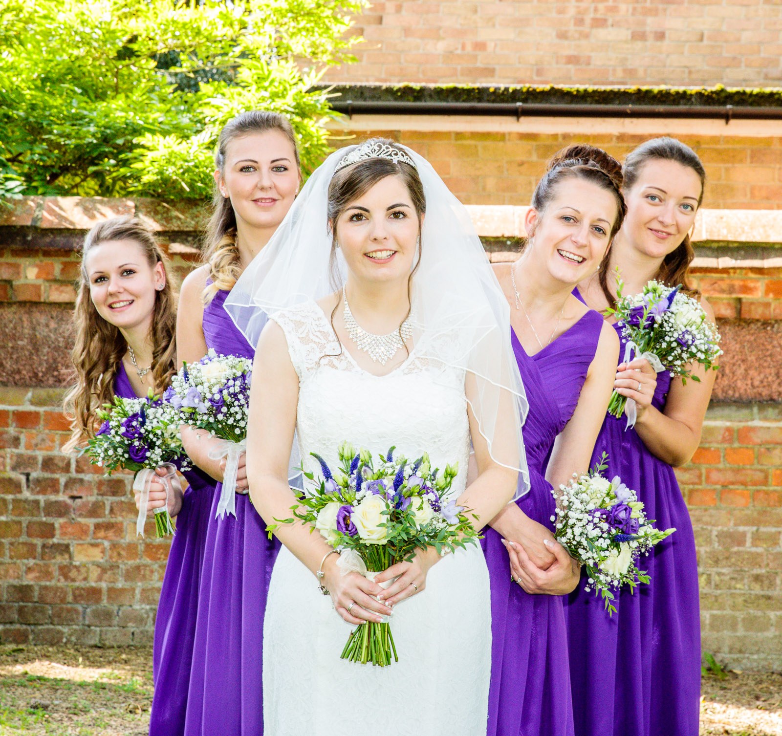 Bride and bridesmaids gathered against the old brick wall of the hotel