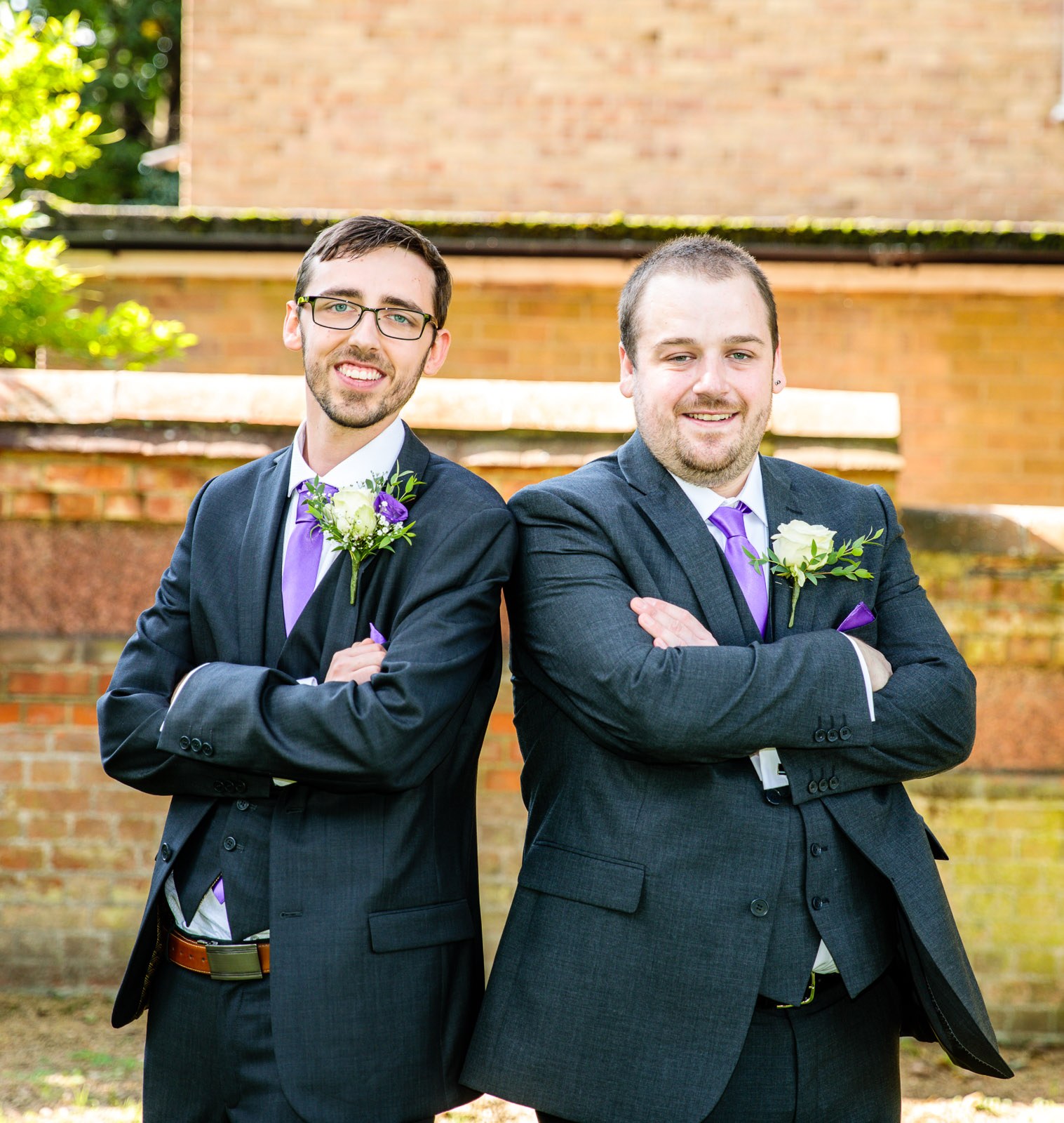 The groom and his best man with folded arms before the brick garden wall