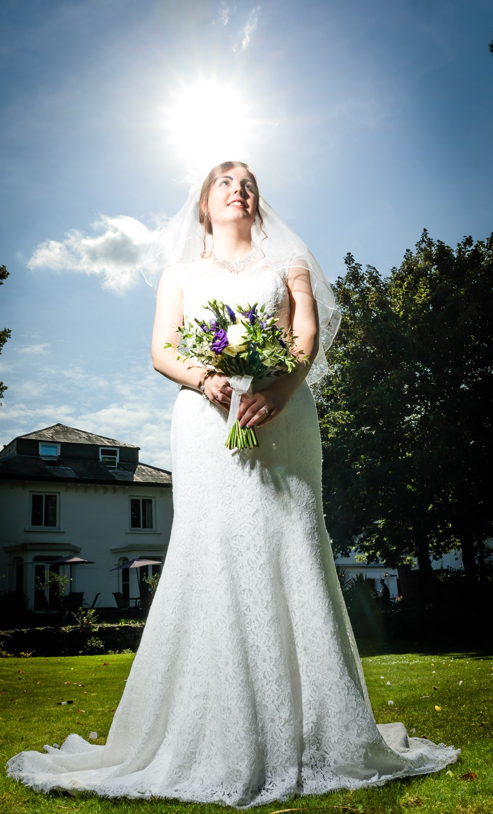 Full-length portrait of the bride on the lawn, the sun flaring behind her