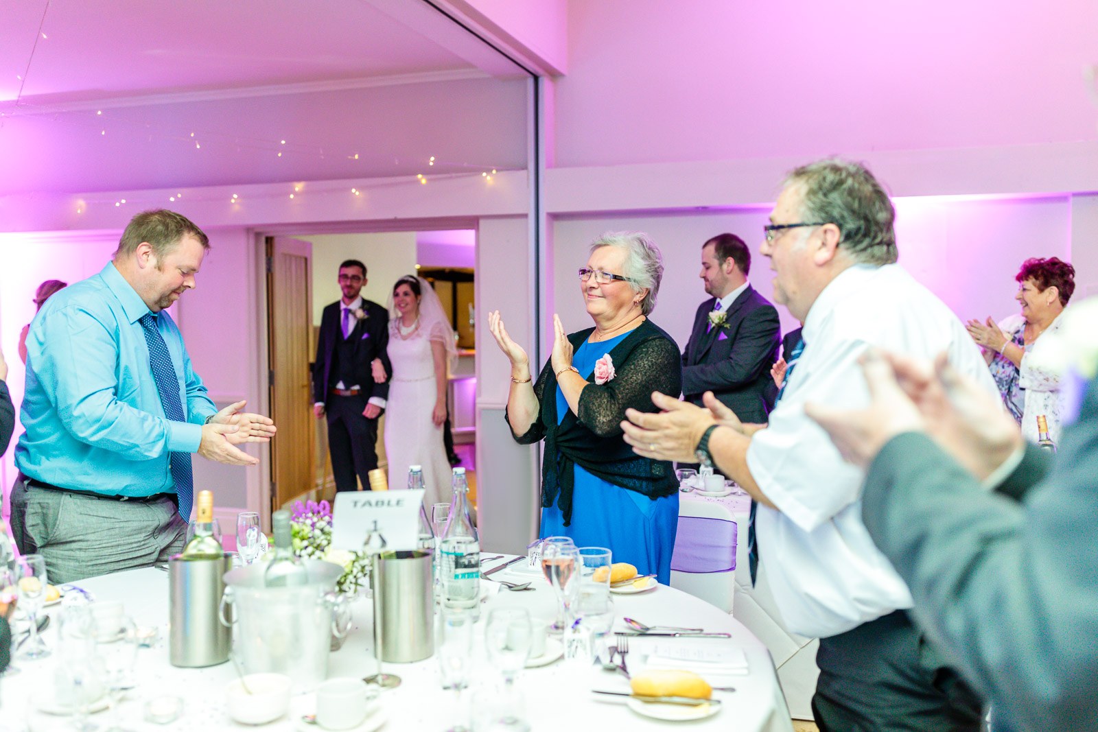 Guests applauding as the couple enter the pink-lit reception room at Hawkwell House Hotel