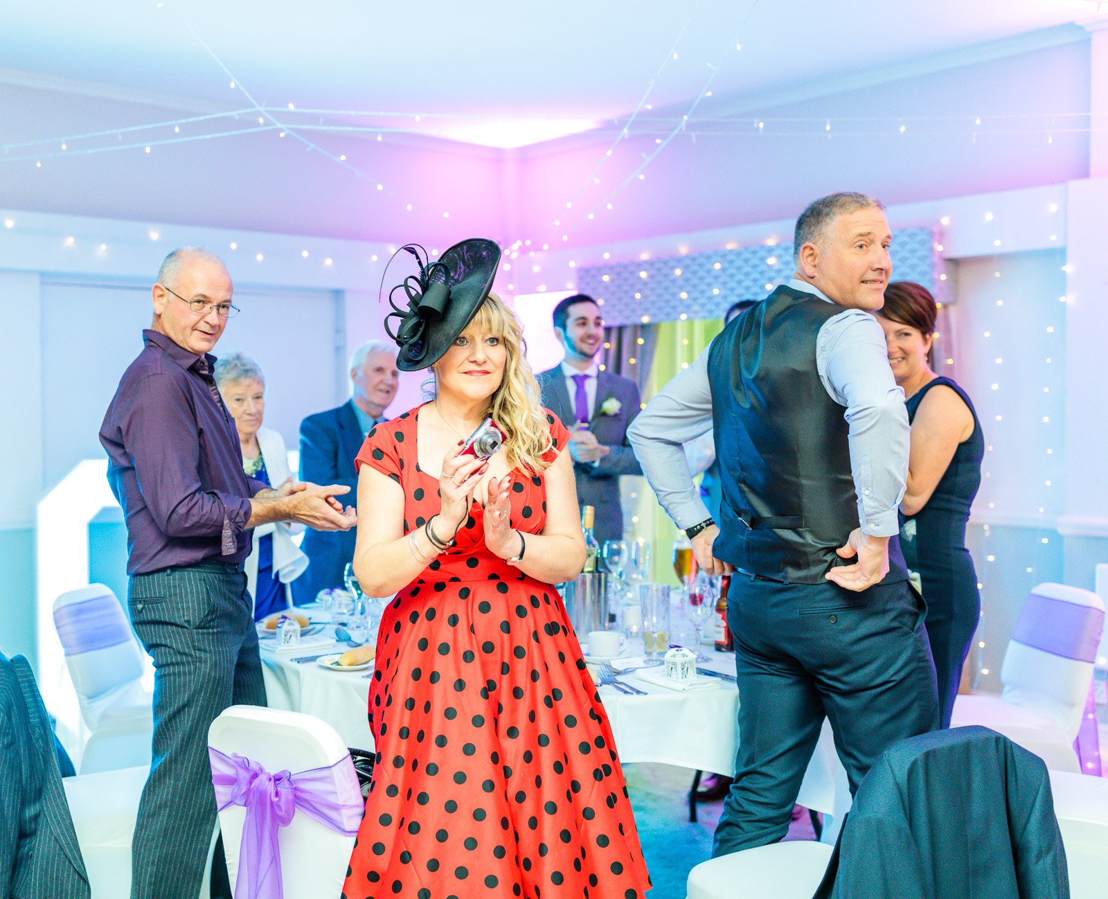 A guest in a red polka-dot dress holding a camera during the reception