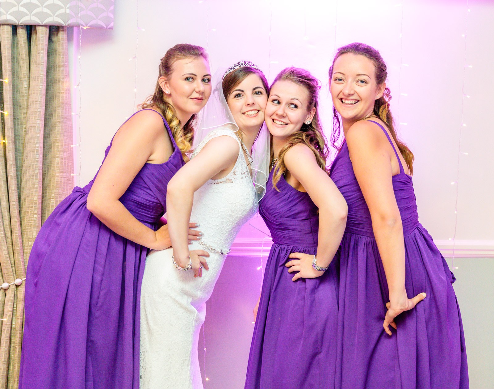 The bride and three bridesmaids posing playfully under pink lighting