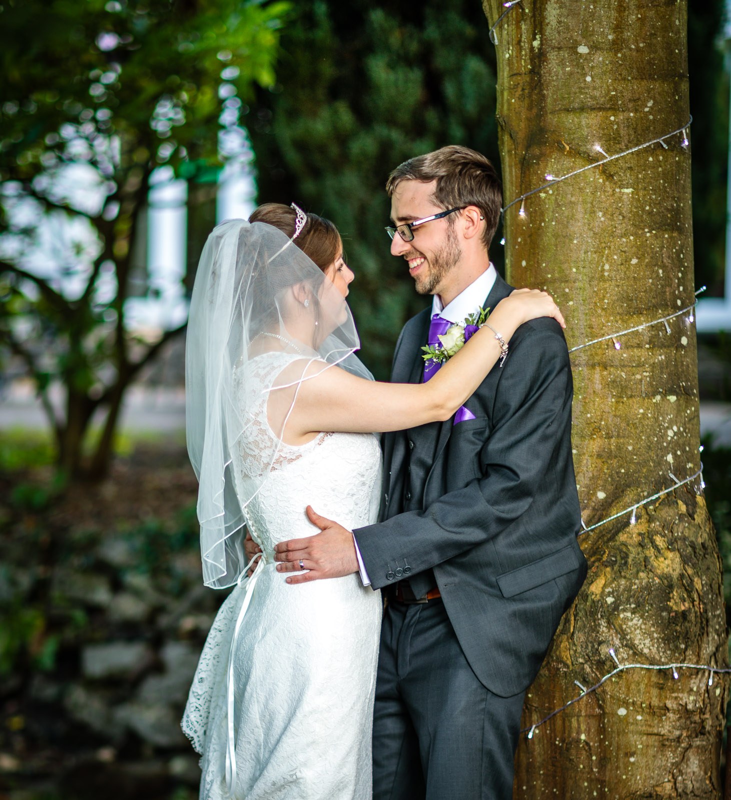 Bride and groom cheek to cheek by the fairy-lit tree at dusk