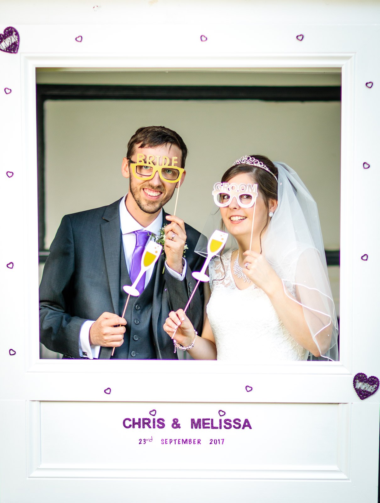The couple larking about with glasses and props in the photo-booth frame