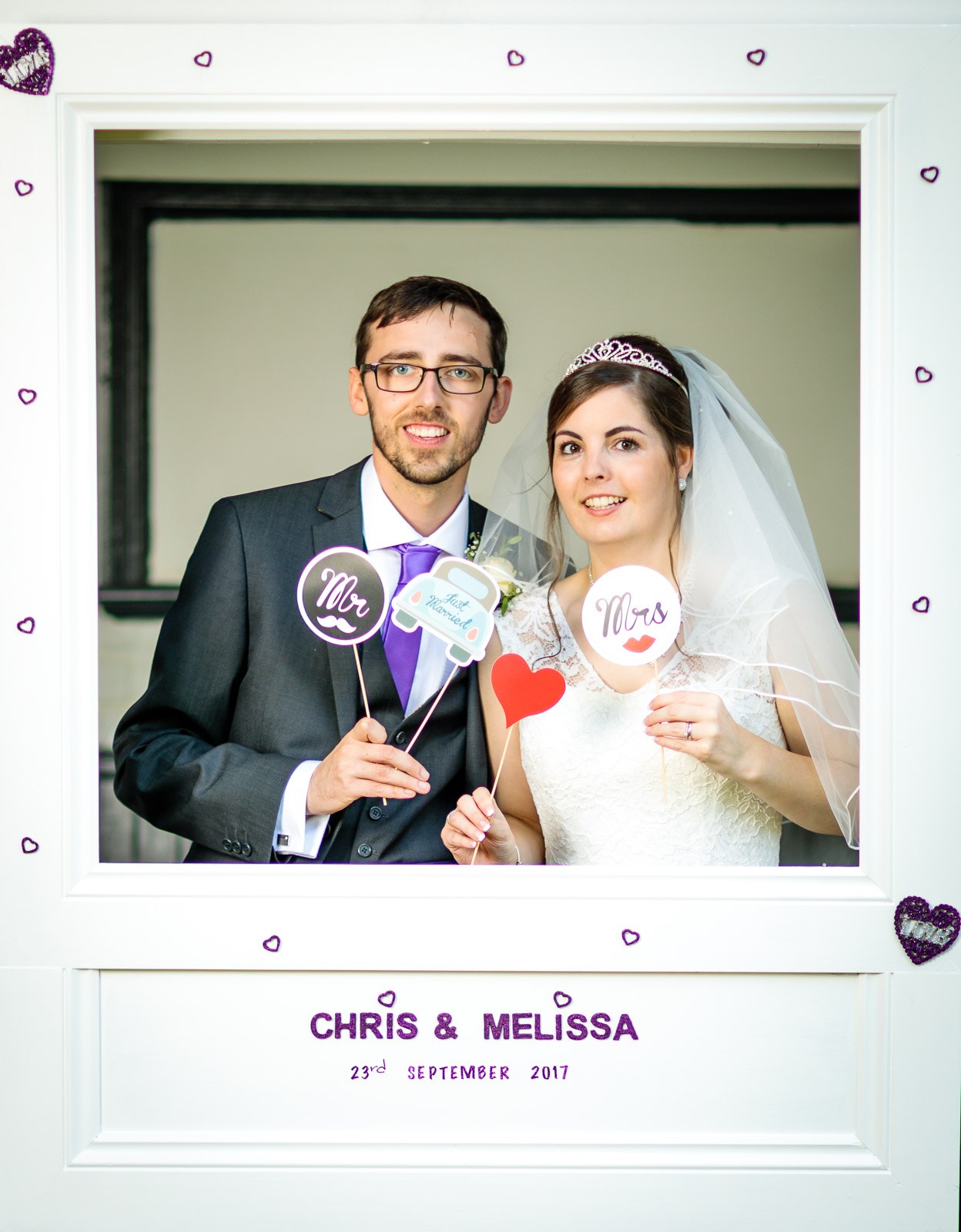 Bride and groom holding up 'Mr' and 'Mrs' props in the photo-booth frame