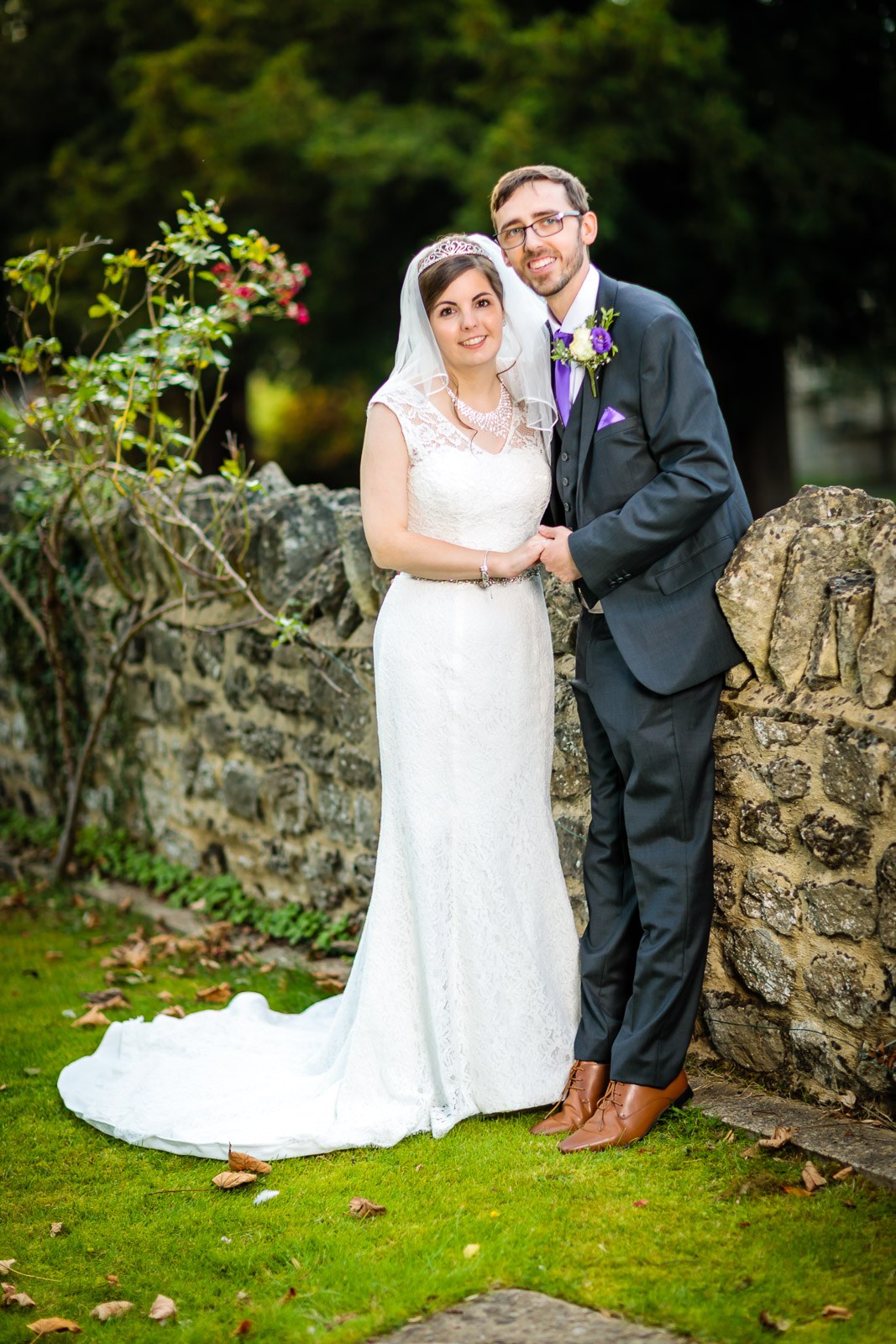 Bride and groom beside a stone wall at the edge of the garden