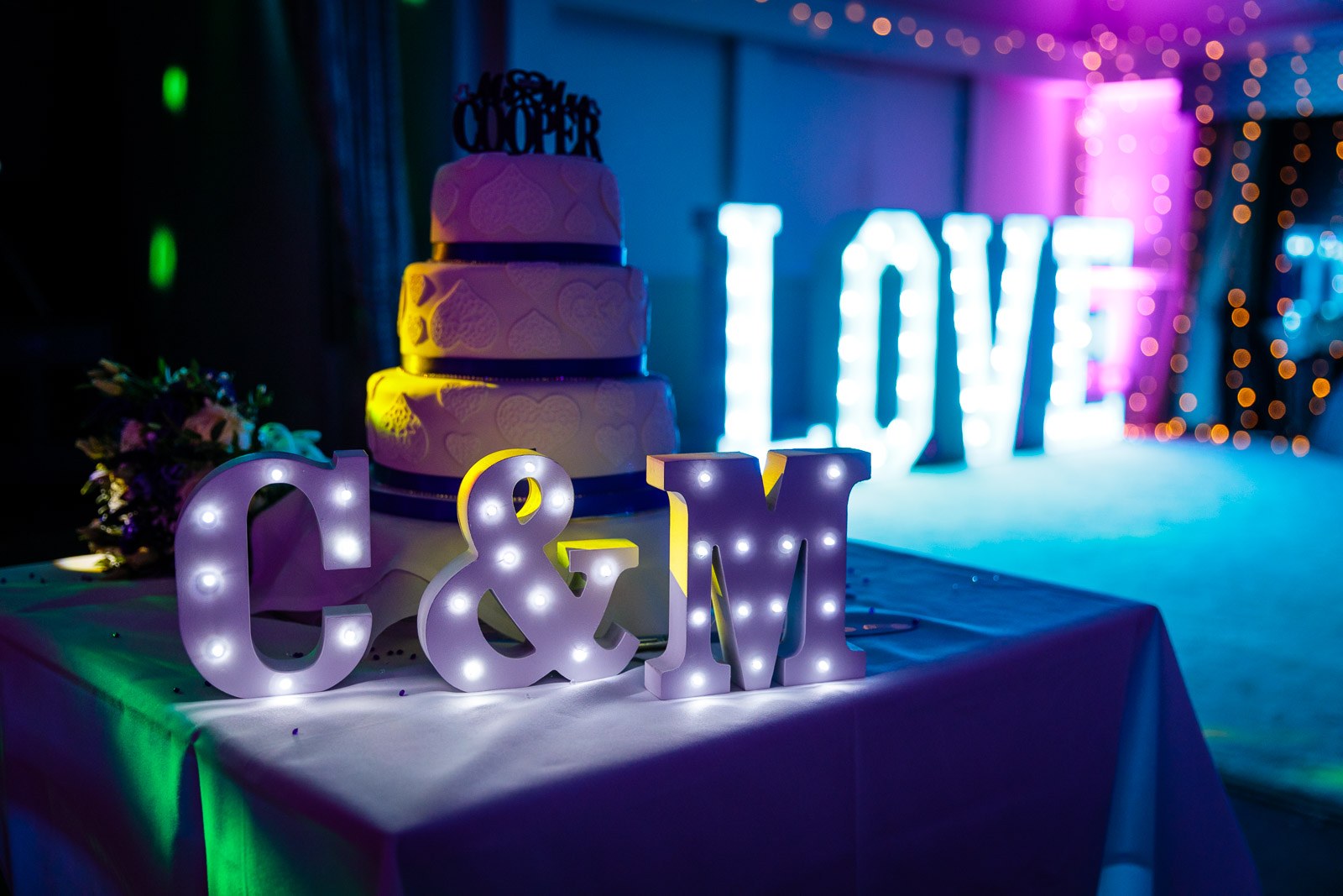 A tiered cake beside light-up letters spelling LOVE and the couple's initials