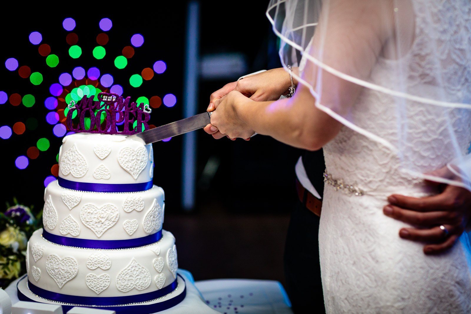 Close-up of the couple's hands cutting the purple-ribboned tiered cake