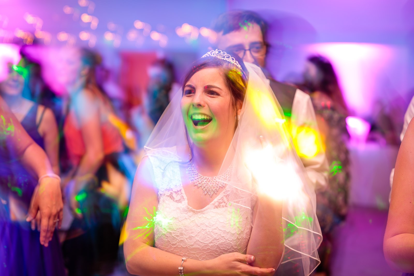 The bride dancing among guests as coloured lights sweep the floor