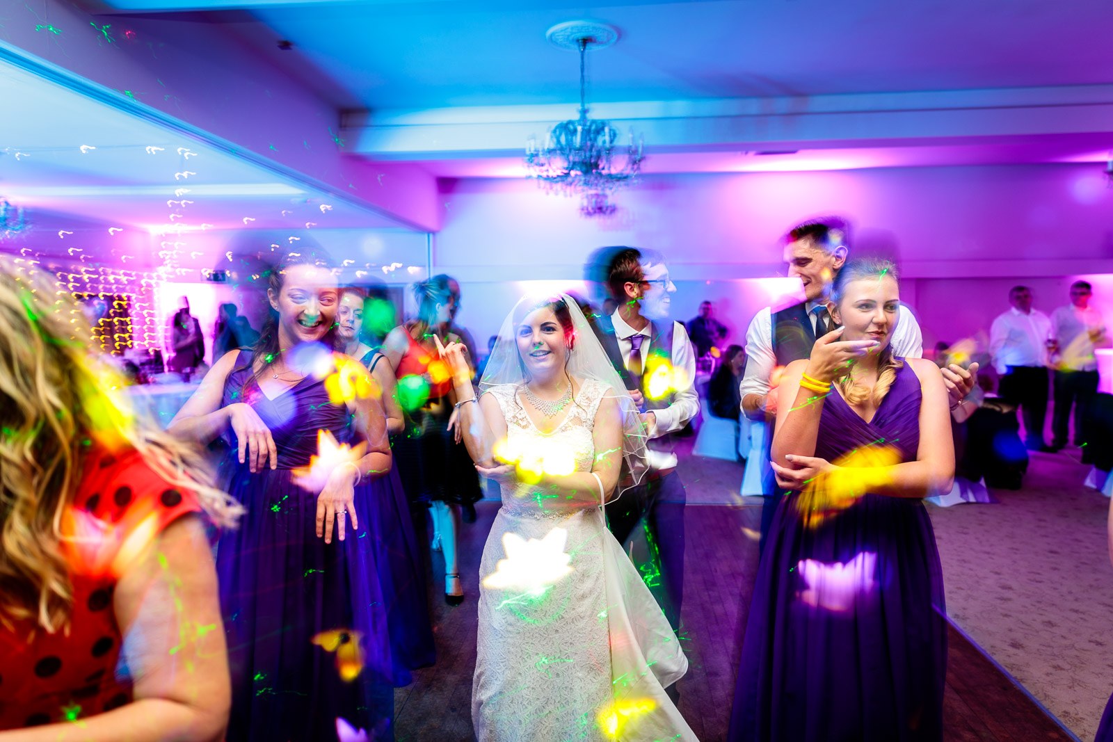 Guests filling the dance floor beneath the chandelier and purple uplighting