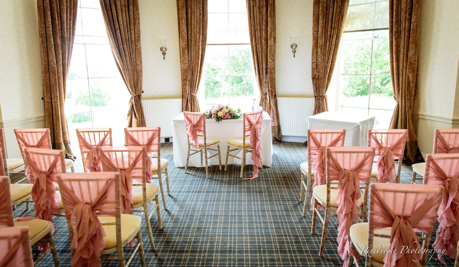 The ceremony room set with pink-sashed chairs before the bay windows at Highfield Park