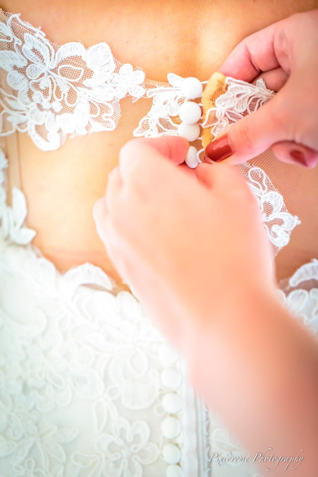 Close-up of hands doing up the buttons at the back of the bride's lace gown