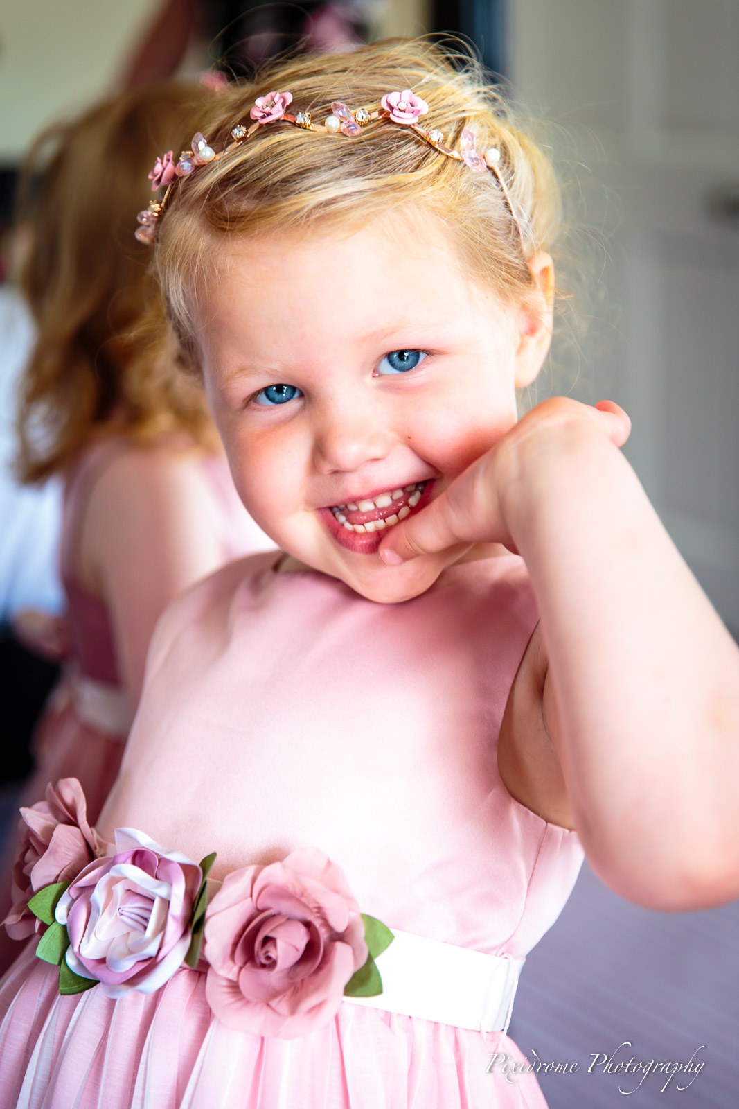 A smiling flower girl in a pink dress with a rose sash