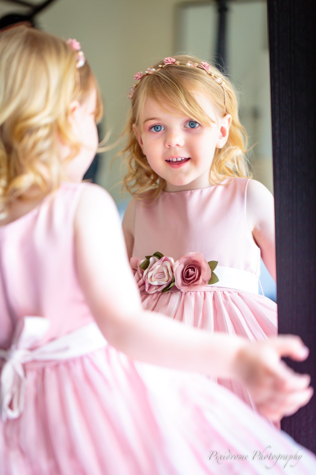 A flower girl in pink twirling before a mirror