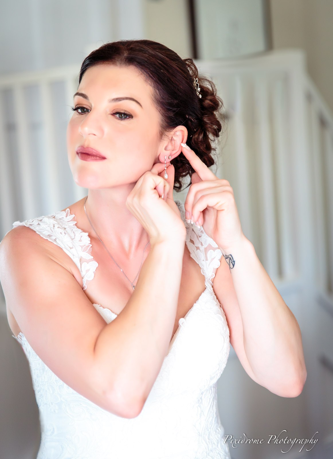 Bride putting in her earrings, hair swept up with a jewelled clip