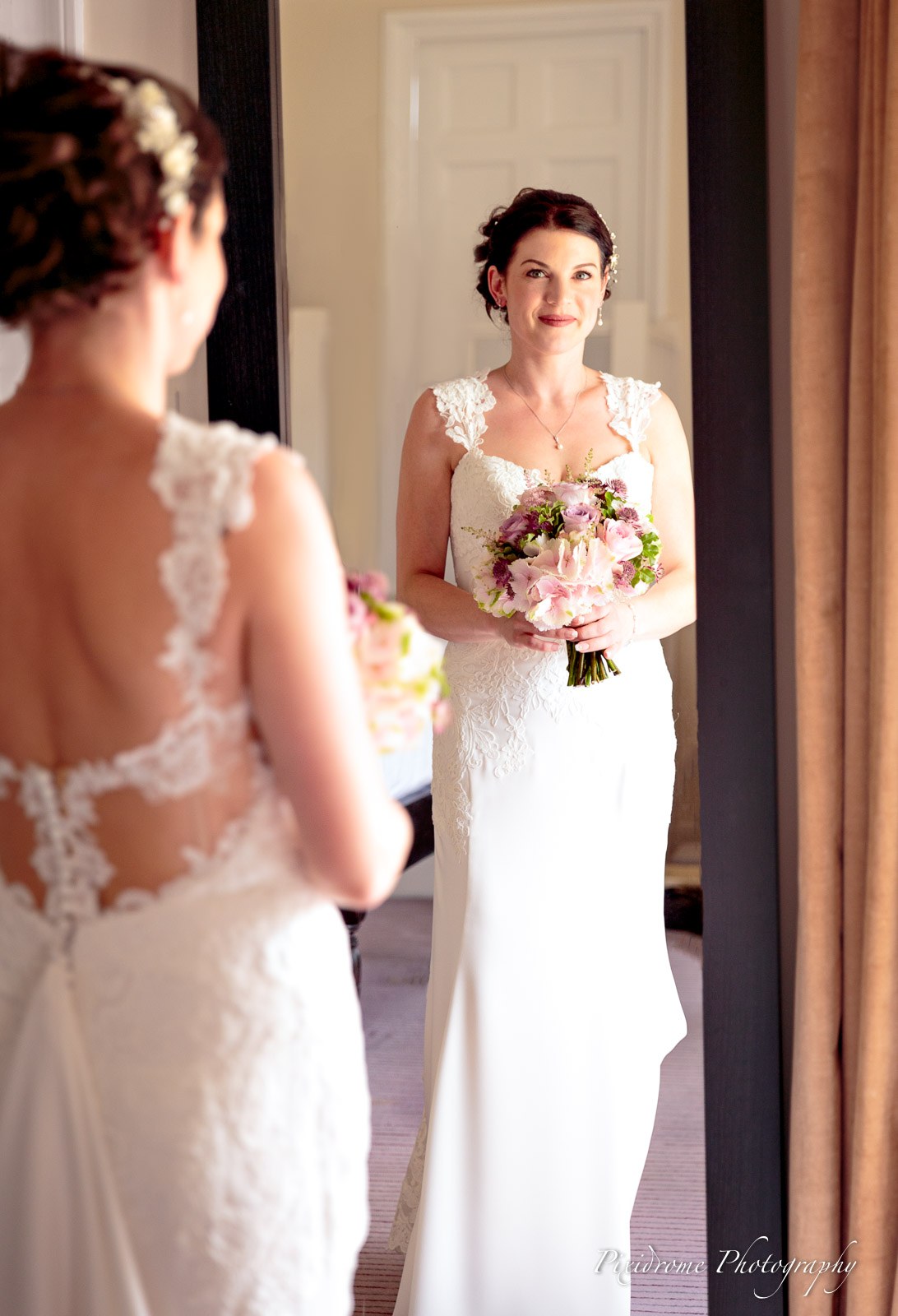The bride reflected in a mirror holding her bouquet, low lace back on show