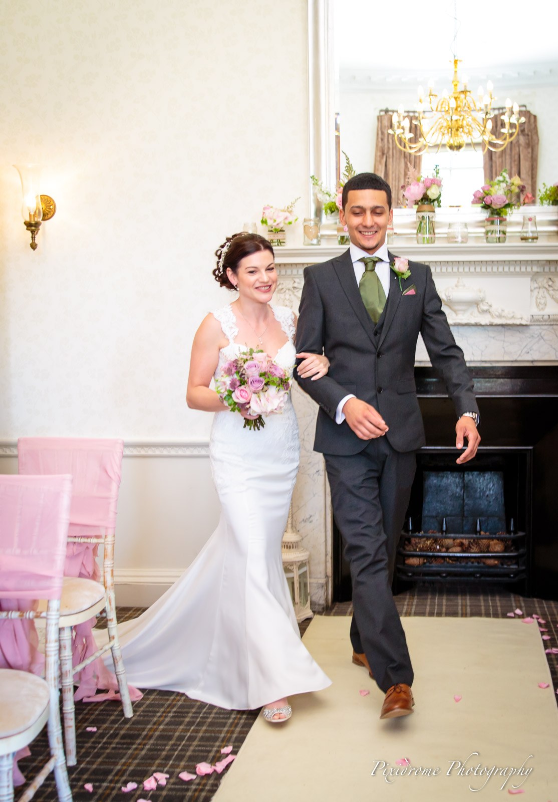 The bride walking up the aisle on the arm of a young man in a grey suit