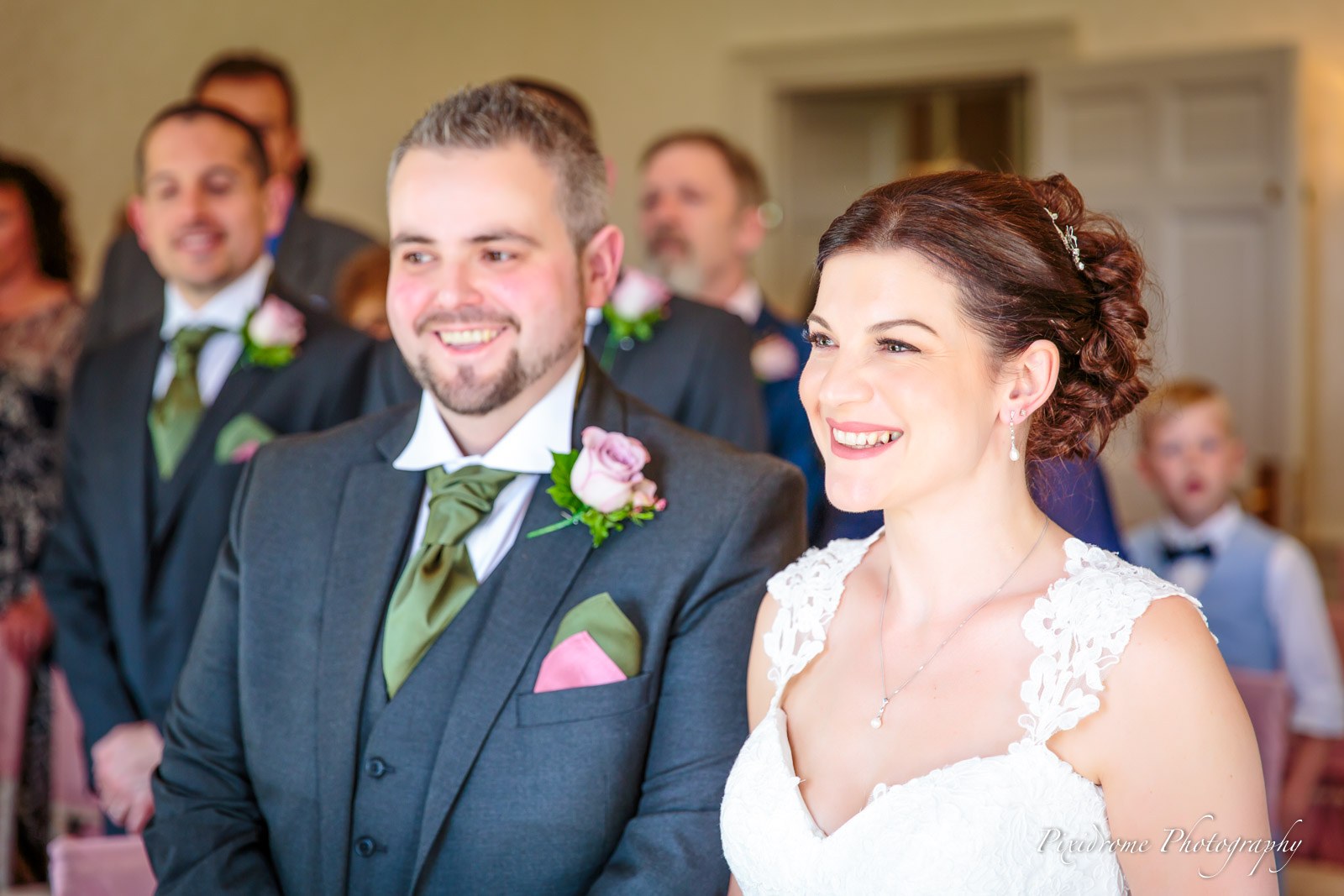 The smiling couple during the ceremony with guests seated behind