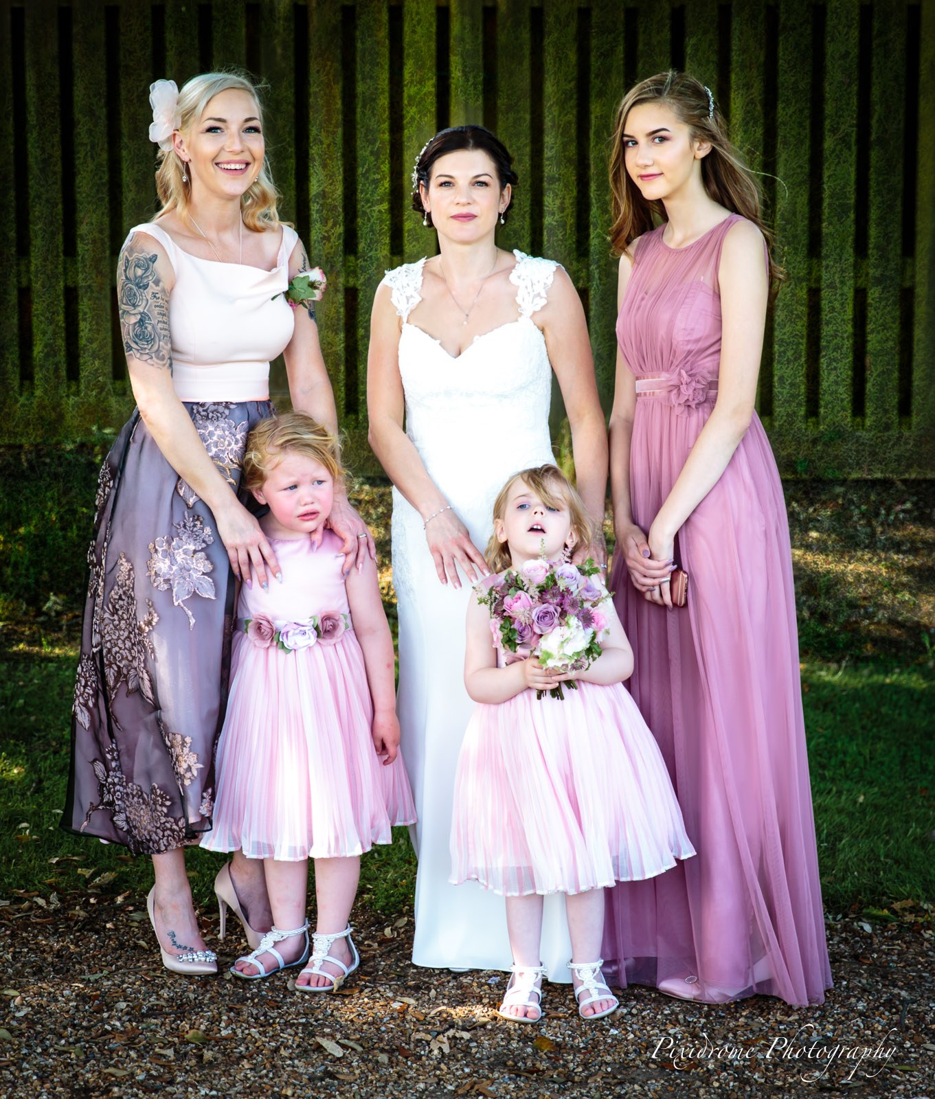 The bride with a bridesmaid, a guest and two flower girls beside a clipped hedge