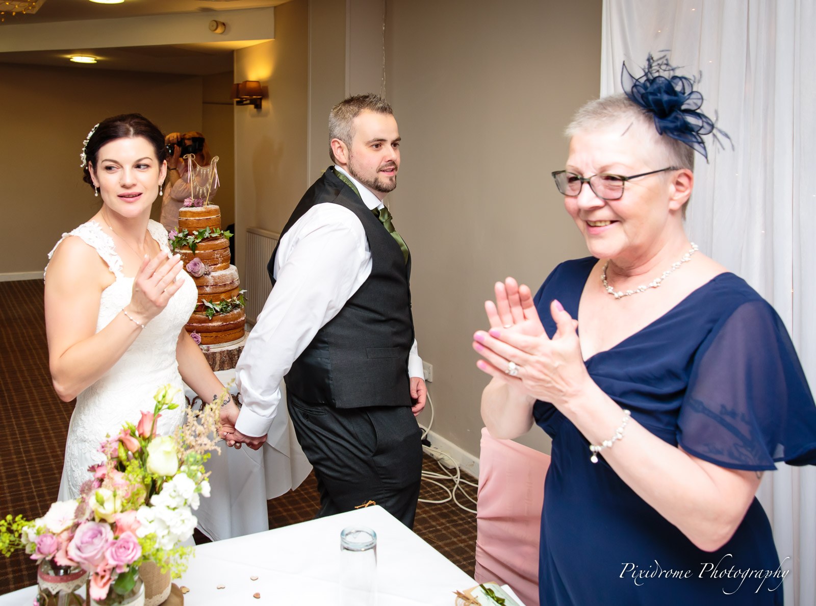 The couple at the cake as an older guest applauds