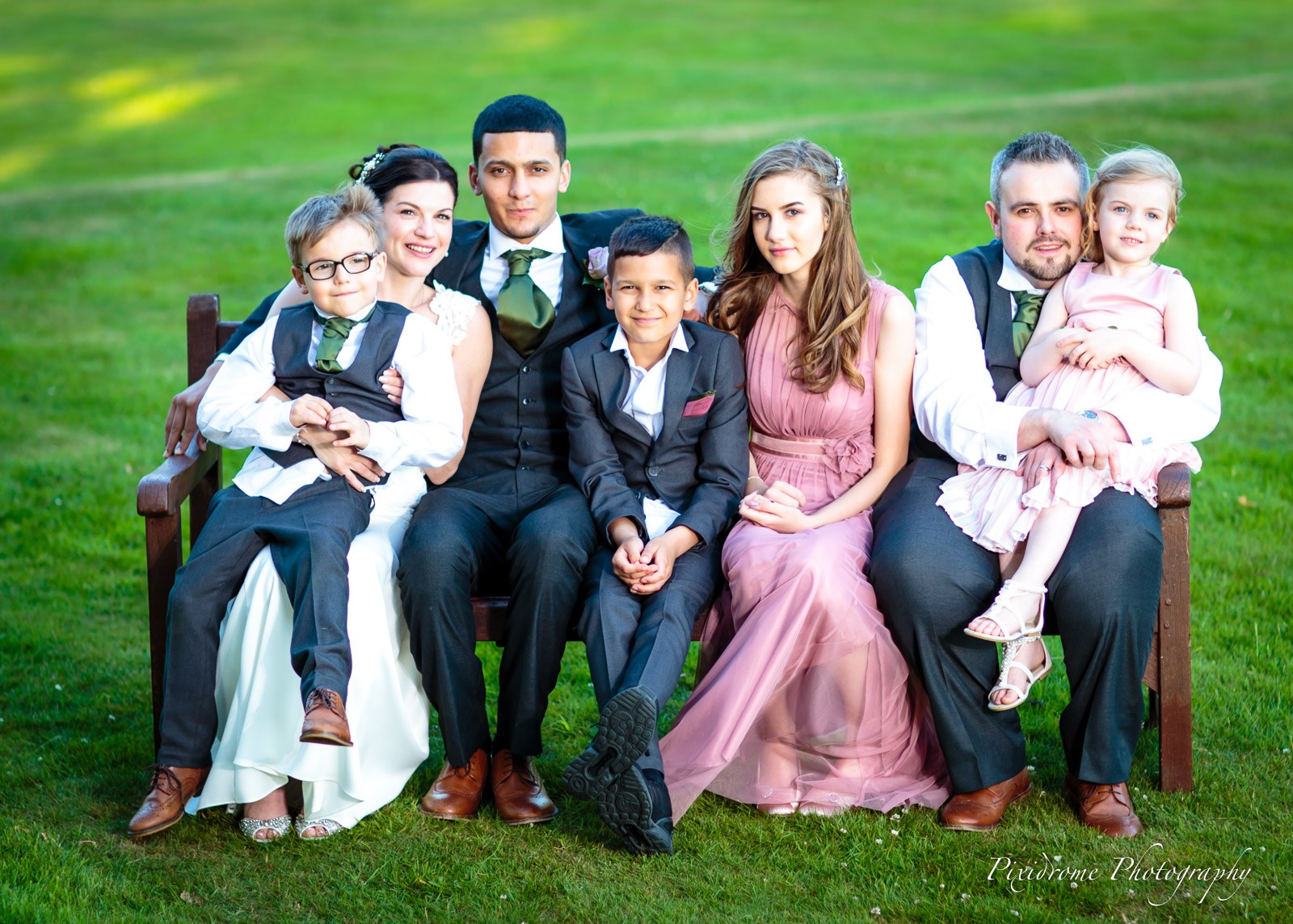 The wedding family gathered on a bench on the lawn