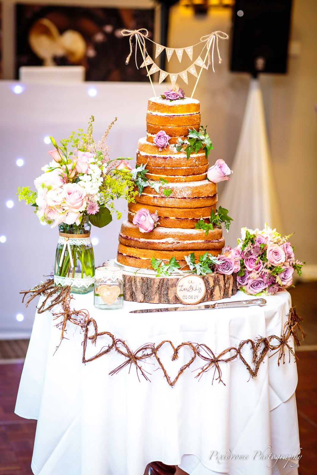 A tiered naked sponge cake dressed with flowers and bunting on a rustic table