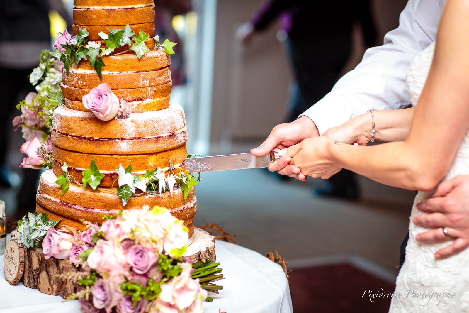 Close-up of hands cutting the flower-trimmed naked cake
