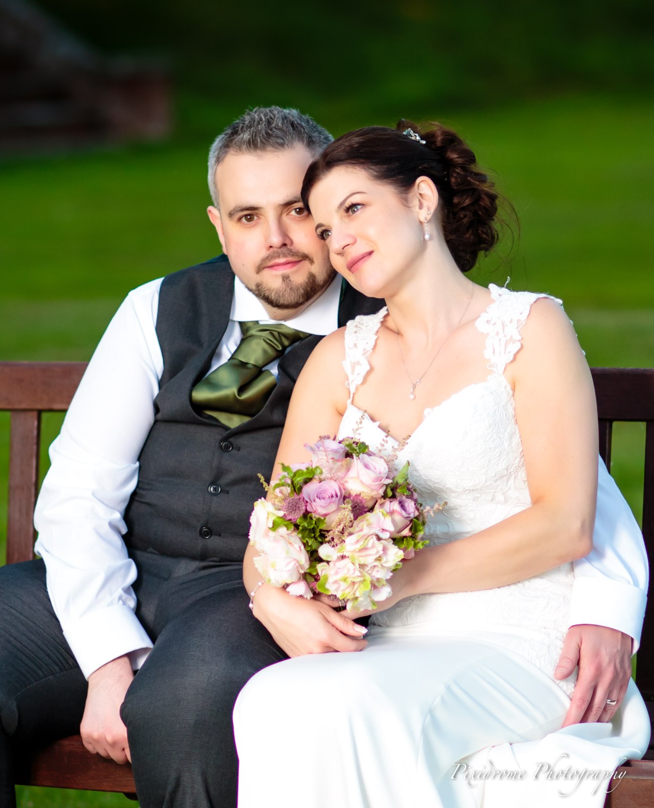 The couple seated on a garden bench, the bride cradling her bouquet