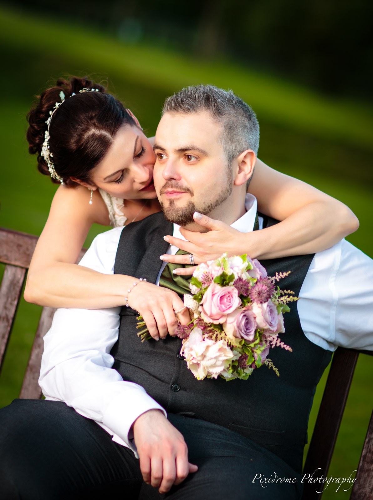 The bride kissing the groom's cheek on a garden bench