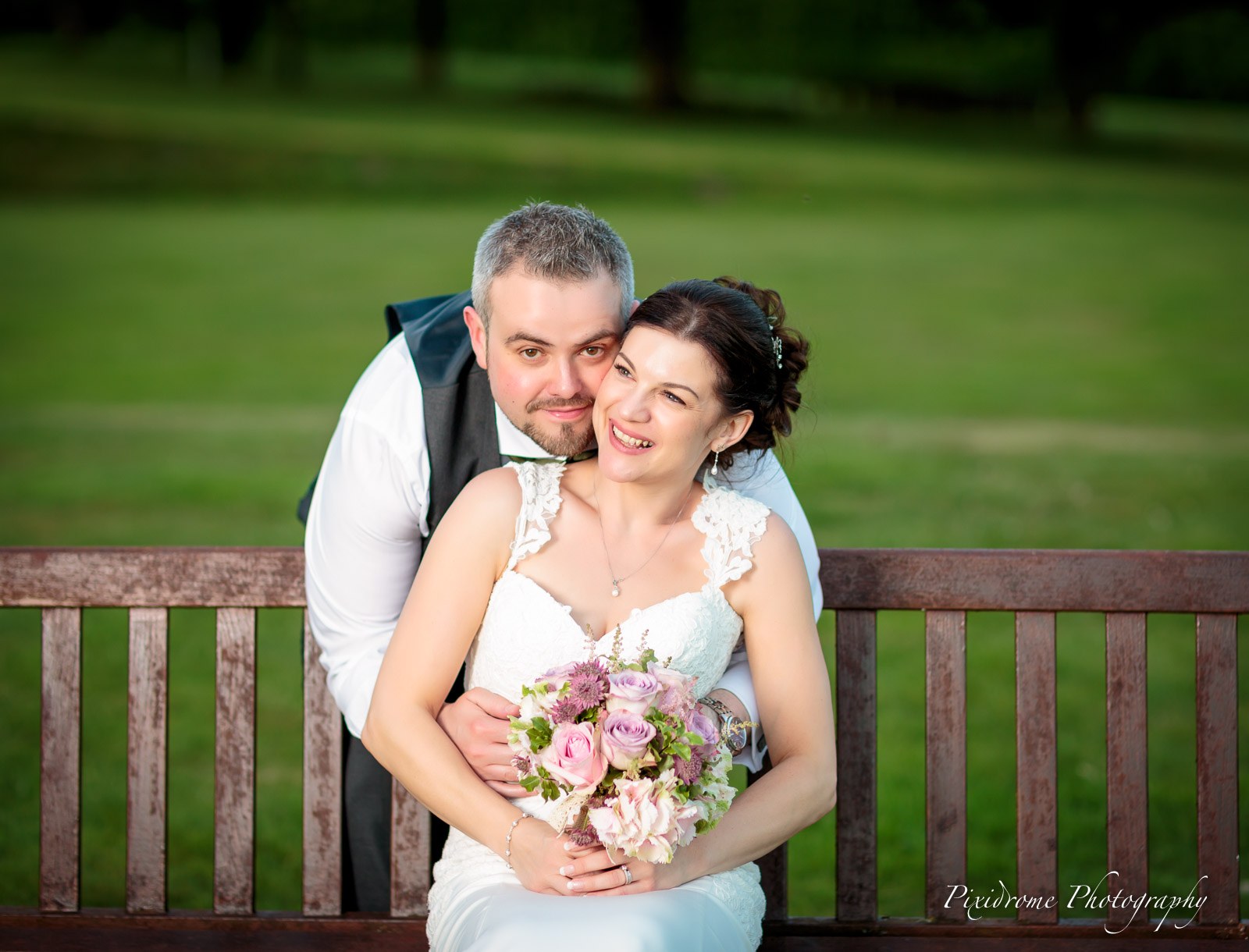 The couple embracing against a wooden bench in the garden
