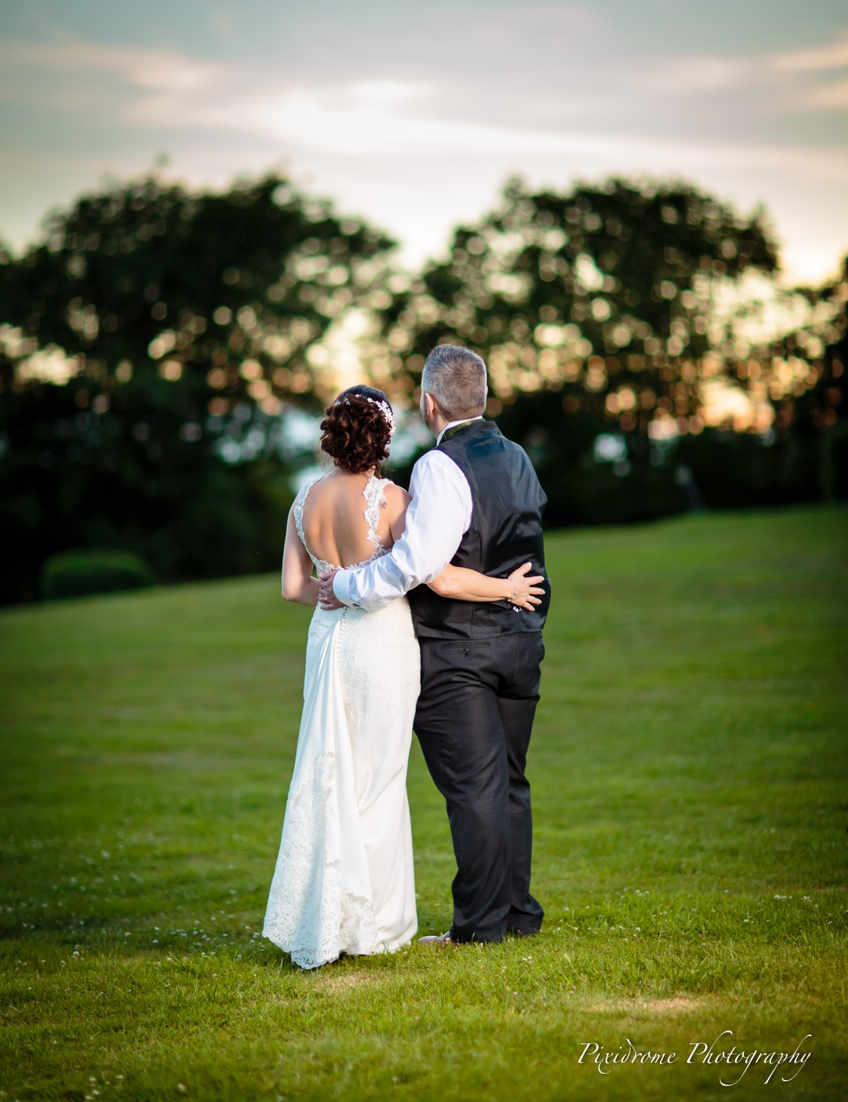 The couple embracing on the parkland lawn as the sun sets