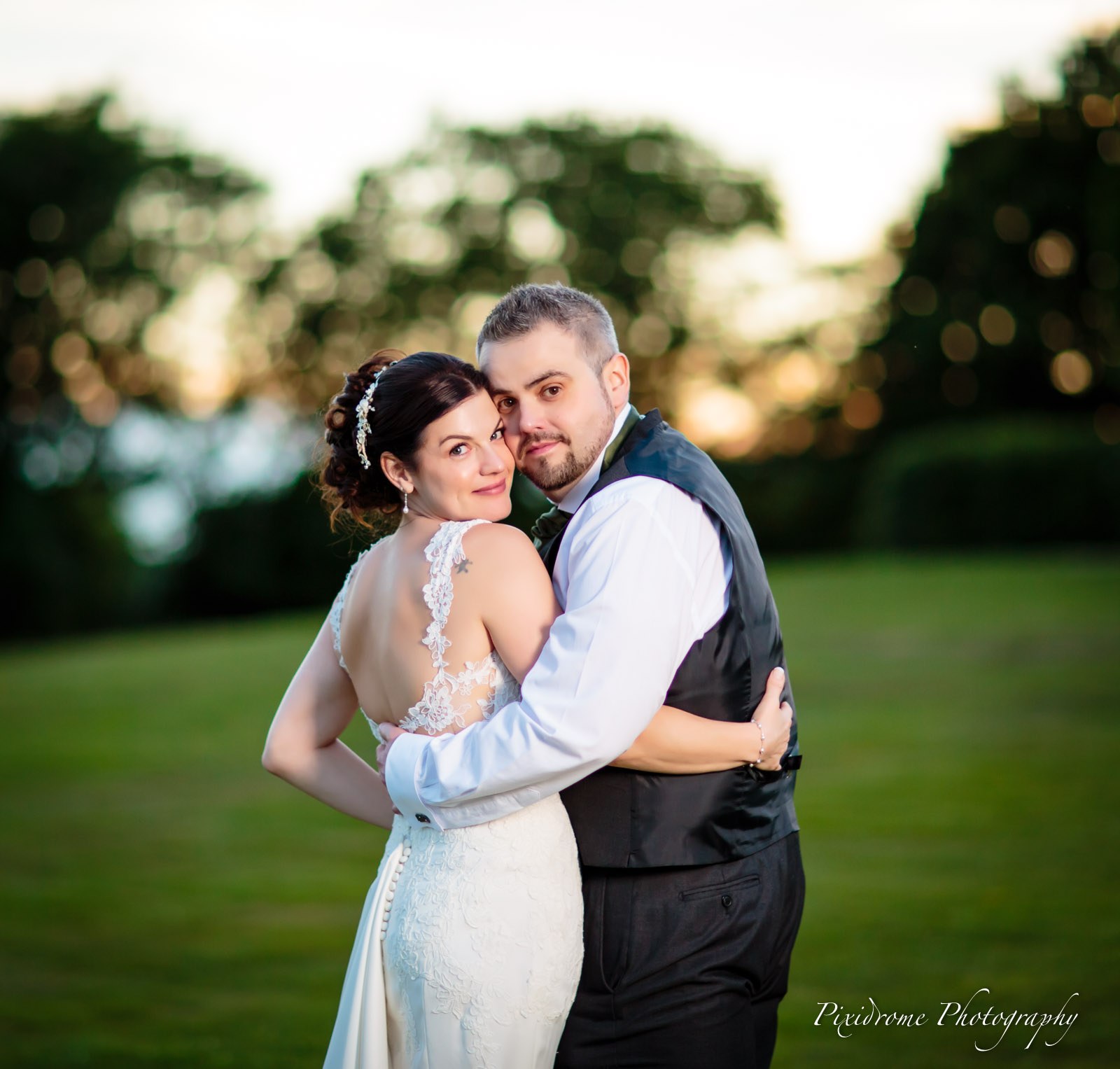 Bride and groom in a close embrace against the sunset tree line
