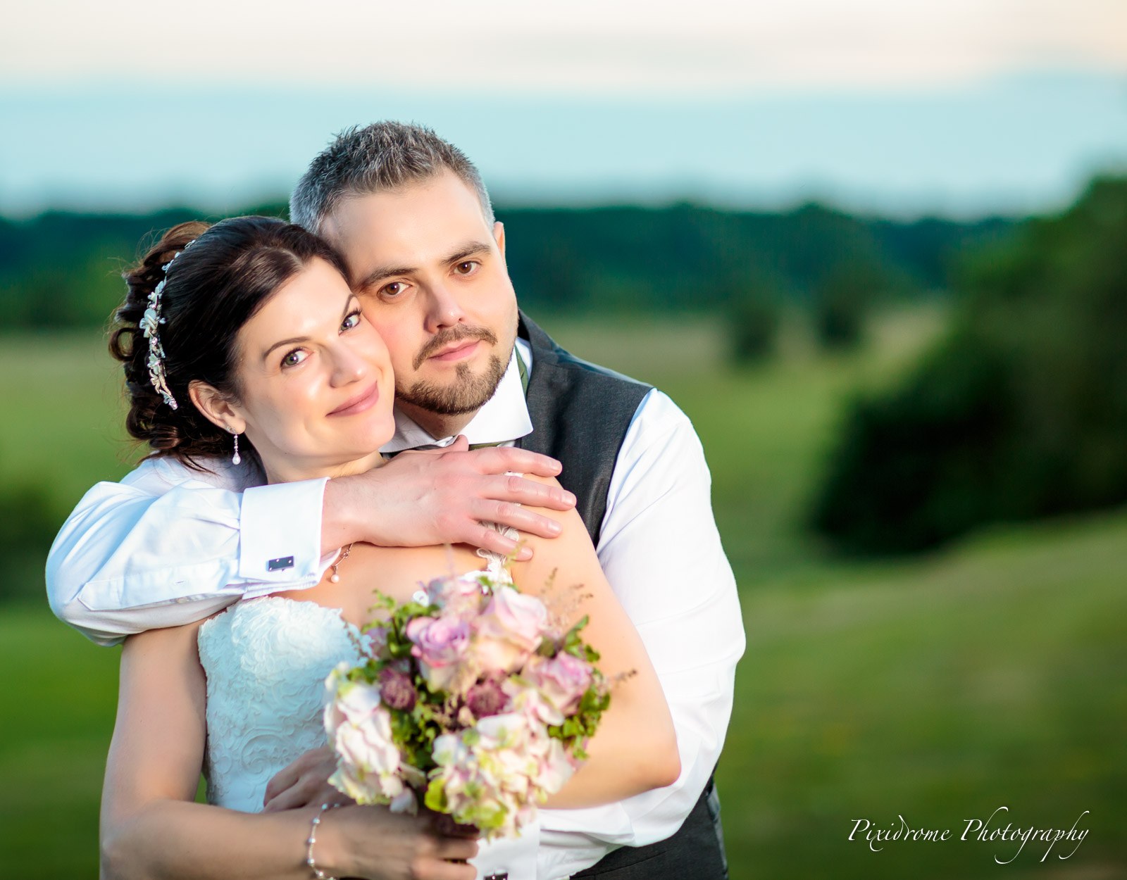 The couple holding the bouquet in the rolling parkland at dusk
