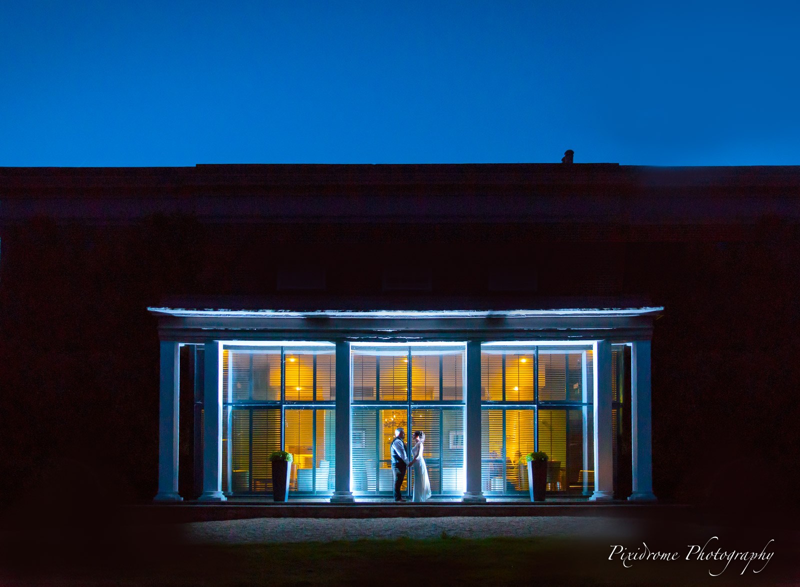 Highfield Park at nightfall, the couple silhouetted in the glowing garden-room windows