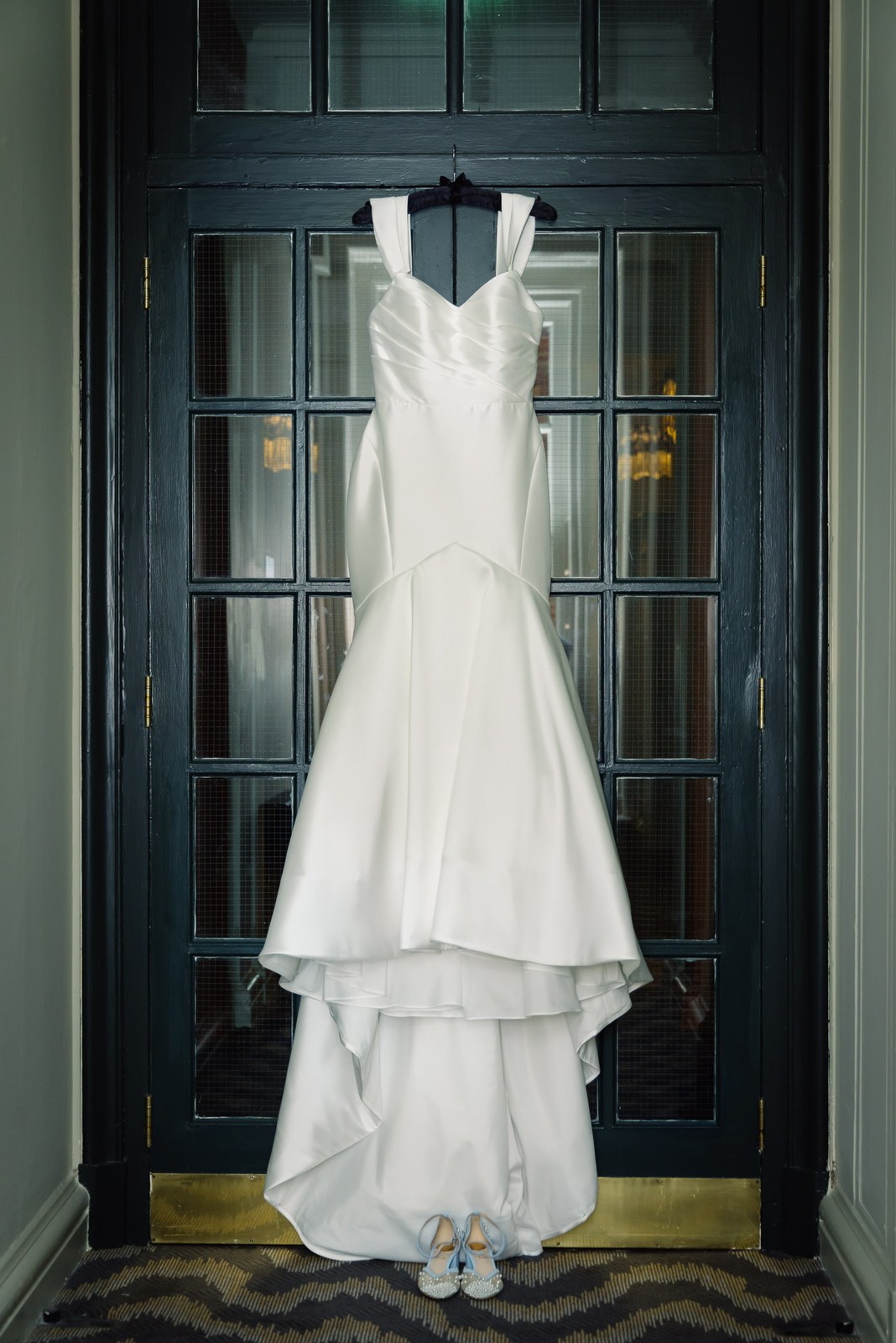 The wedding gown hanging on a dark panelled door with the bride's shoes below