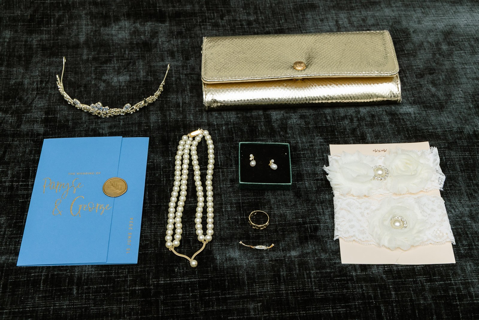 A flat-lay of bridal details: tiara, pearls, earrings, ring, garters and a gold clutch