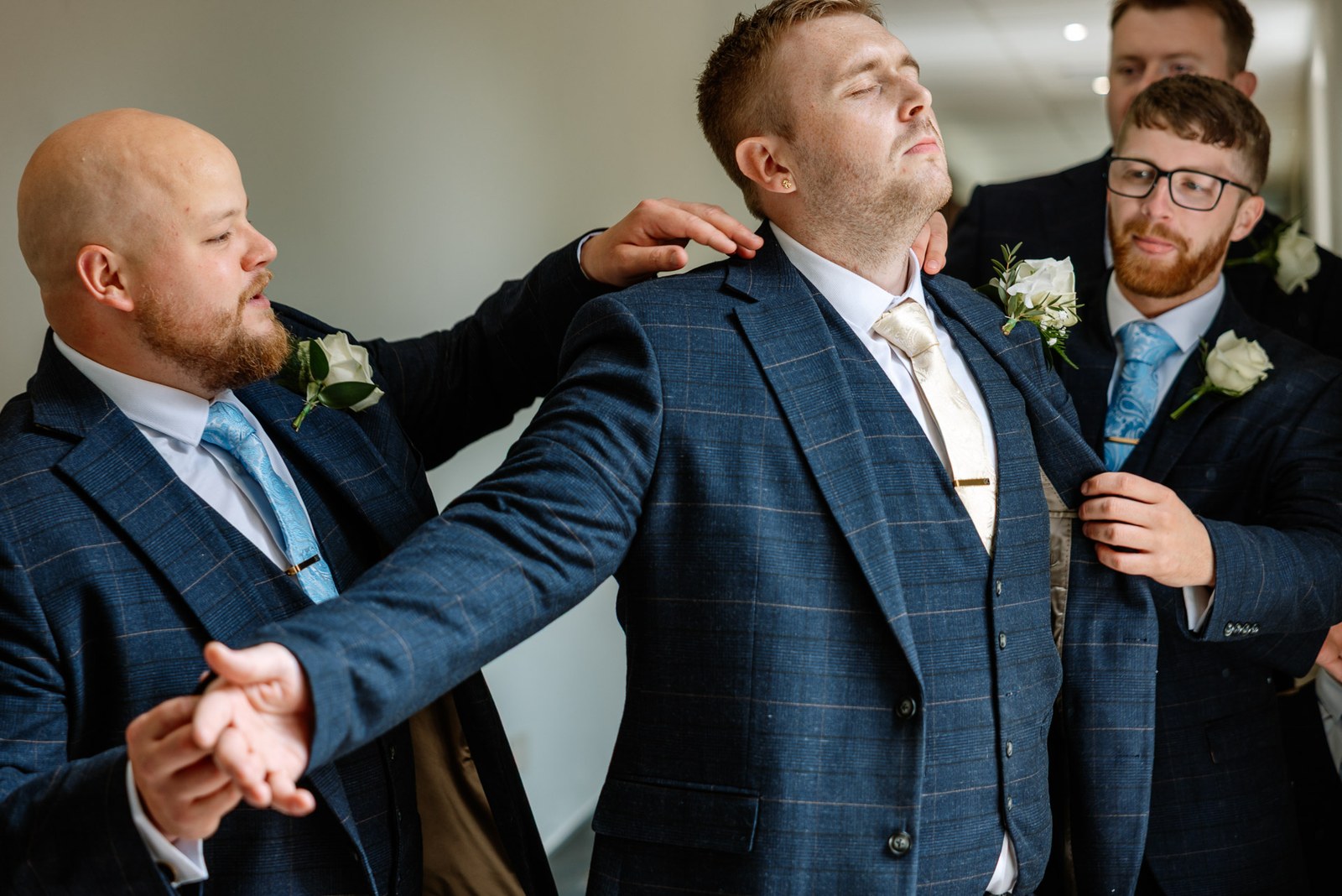 Groomsmen in navy check suits helping the groom to dress