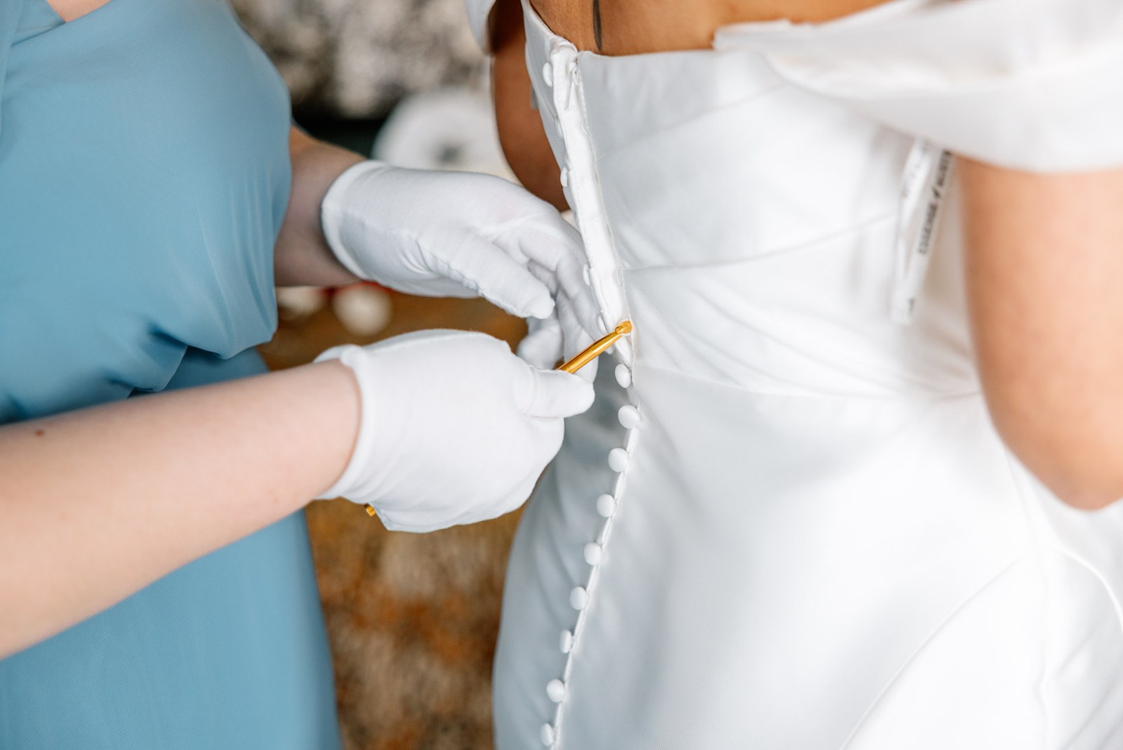 White-gloved hands doing up the covered buttons at the back of the gown