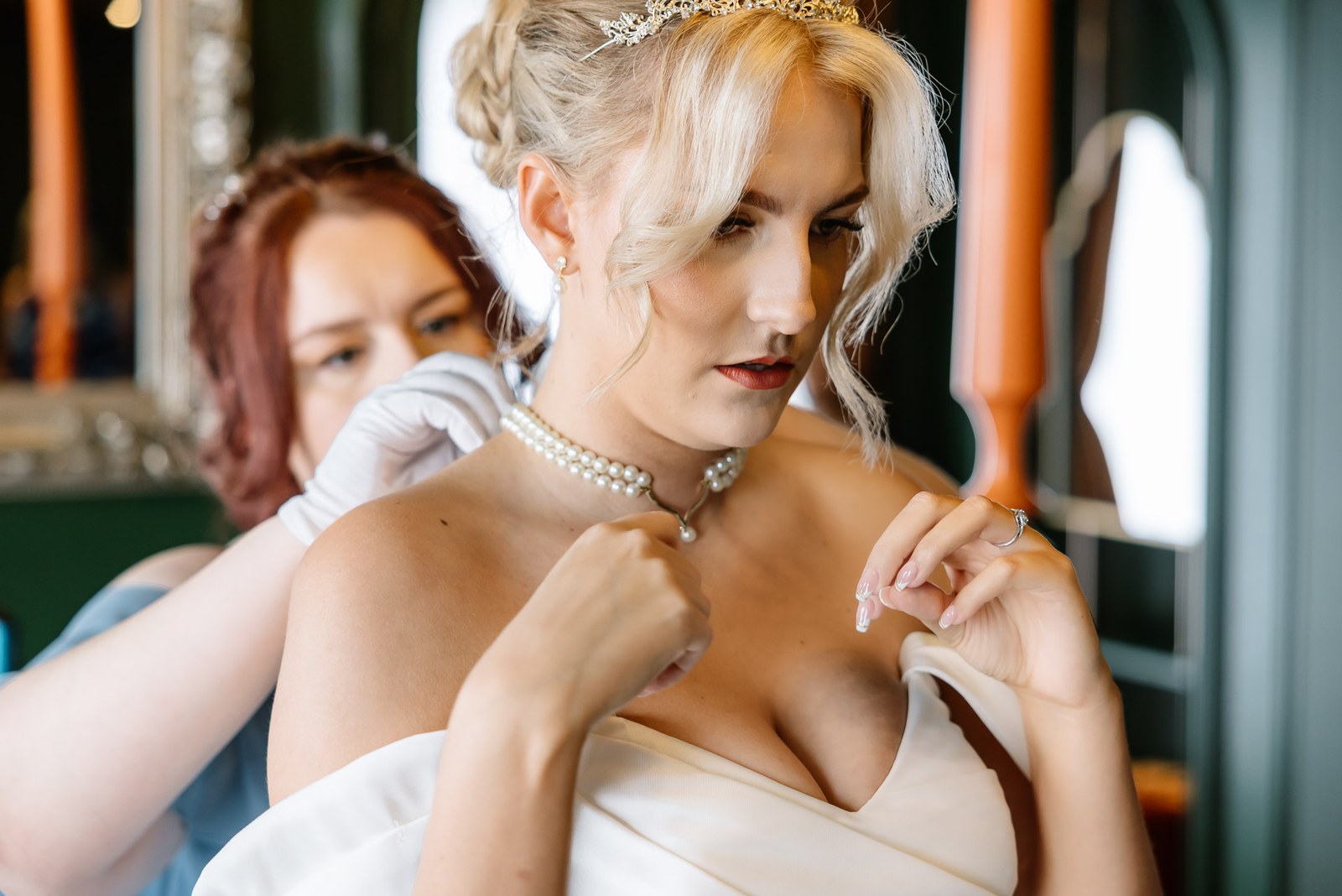 A bridesmaid fastening a pearl necklace at the bride's neck