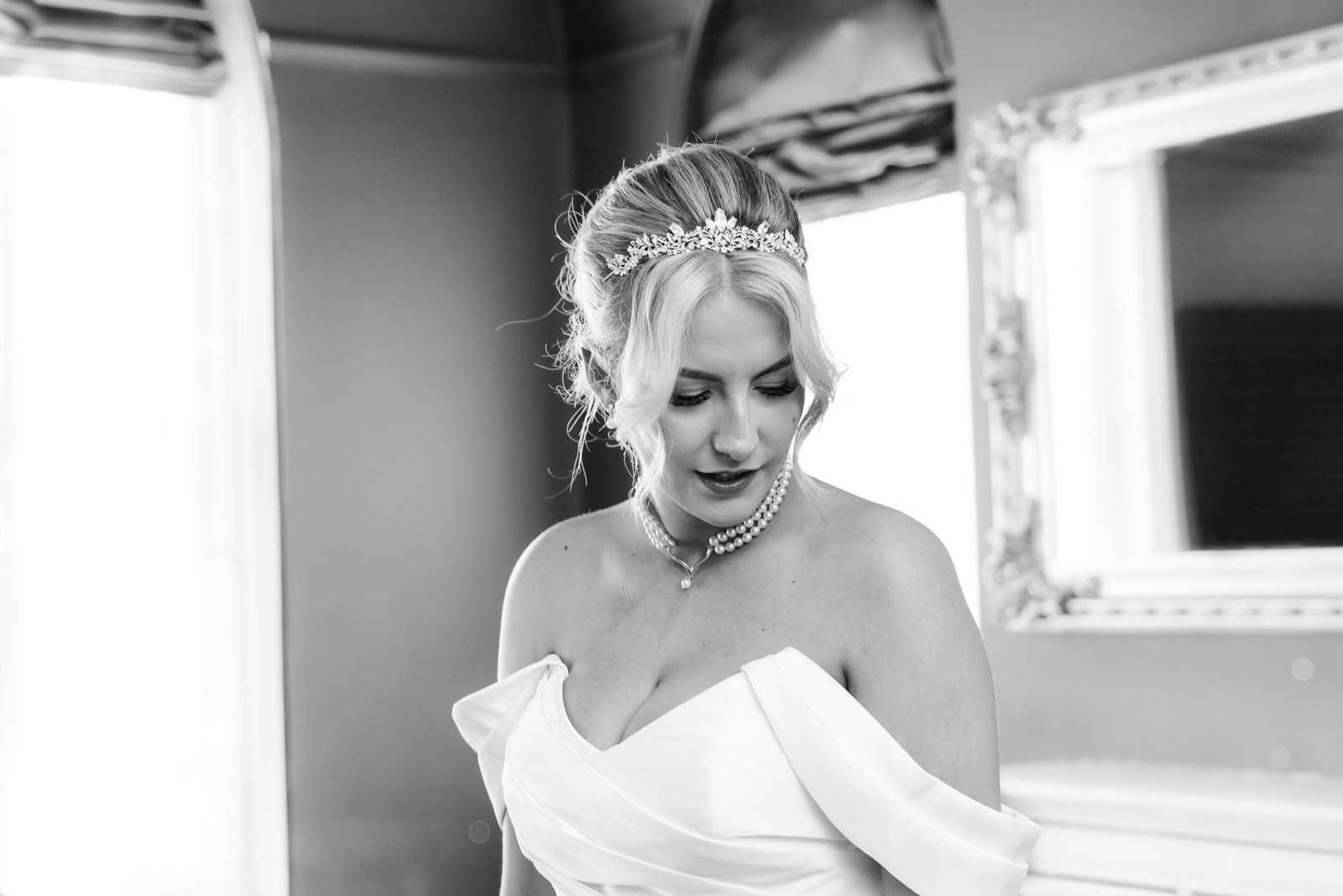 Black-and-white portrait of the bride looking down in her off-shoulder gown