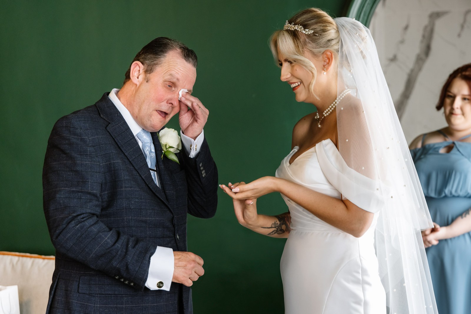 The father of the bride wiping away a tear as the bride laughs beside him