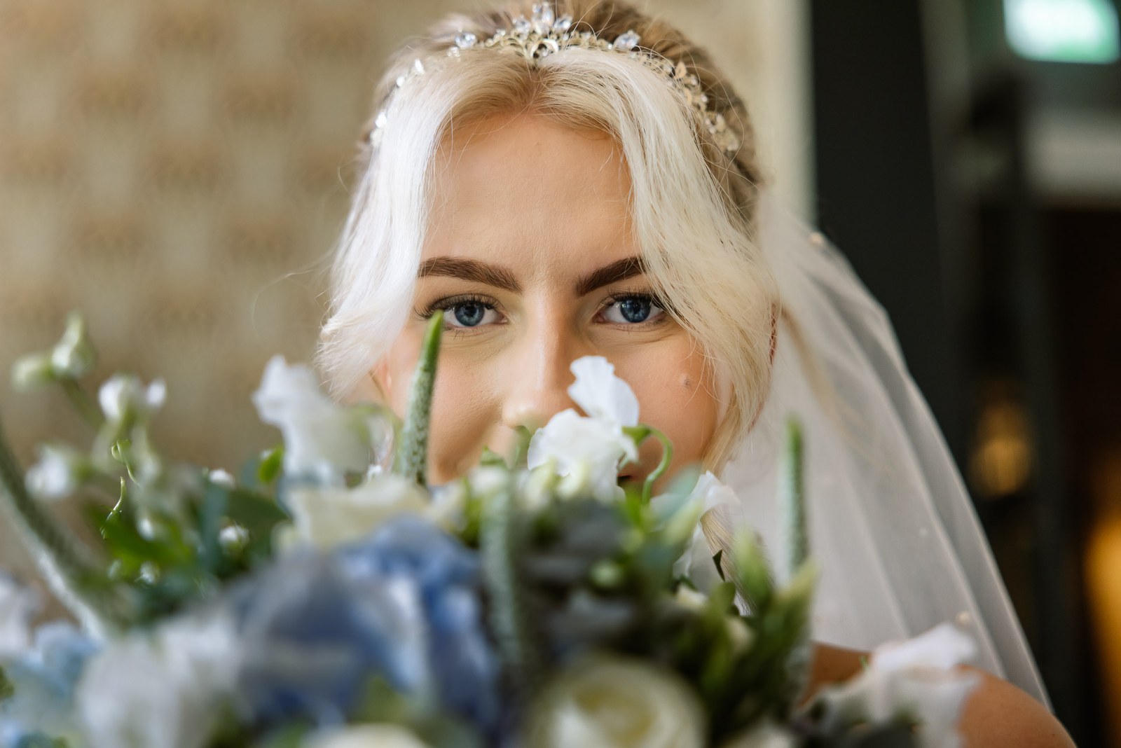 The bride peeking over the top of her blue and white bouquet