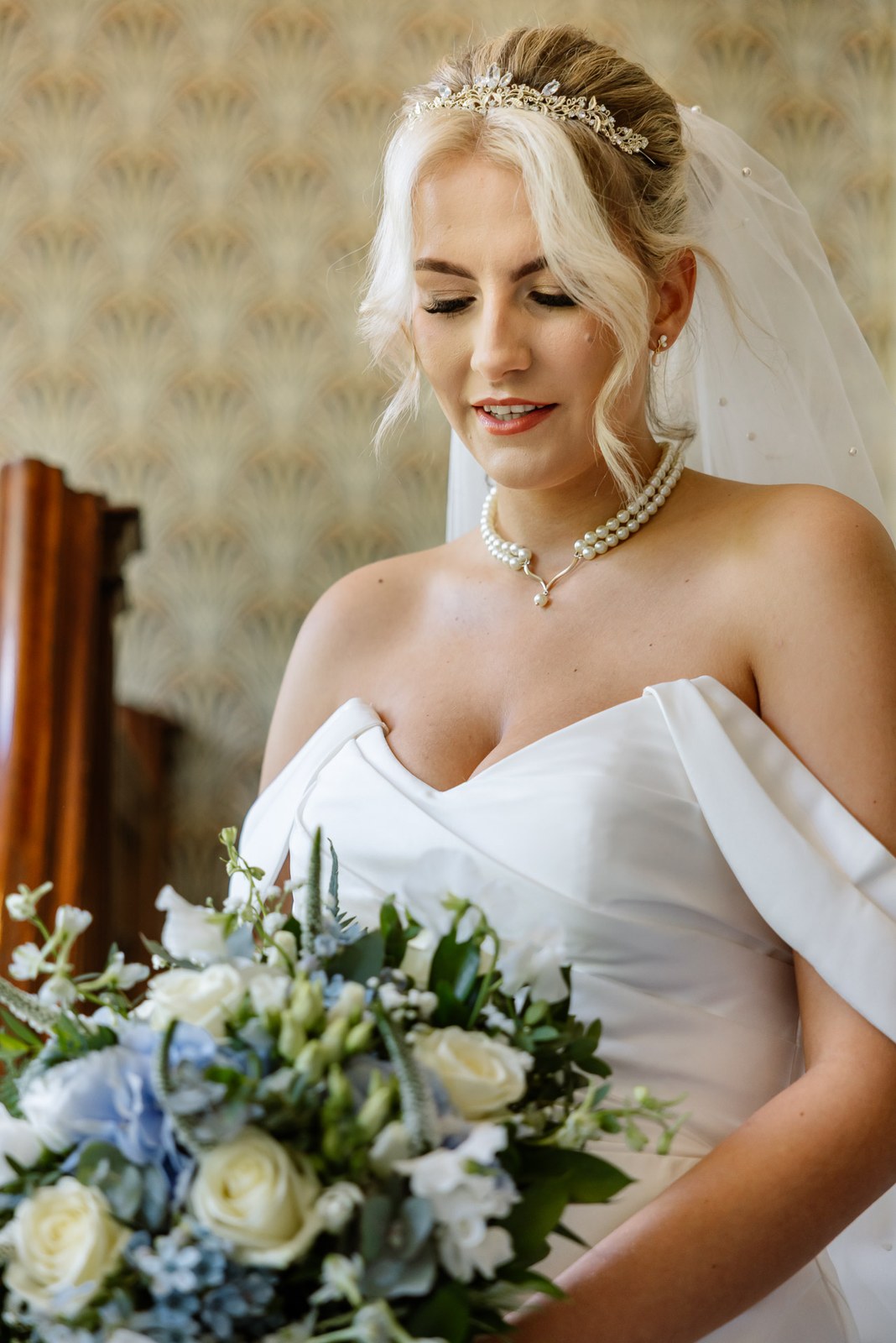 Portrait of the bride with her bouquet against patterned wallpaper